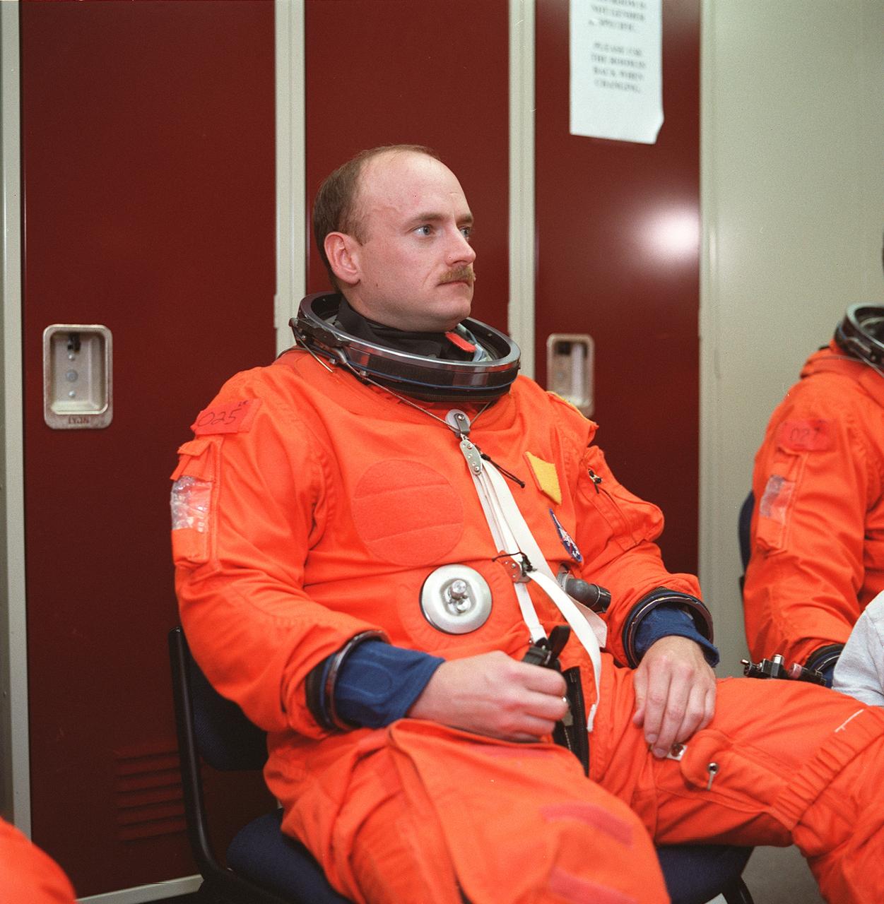 S99-08646 (24 May 1999) --- Astronaut Scott J. Kelly, pilot, listens to a briefing by a member of the crew training staff during a session of emergency bailout training in the Systems Integration Facility at the Johnson Space Center (JSC). Kelly, wearing a training version of the partial-pressure launch and entry garment, and his six STS-103 crew mates are currently in training for the third servicing visit to the Hubble Space Telescope (HST) since its 1990 deployment.