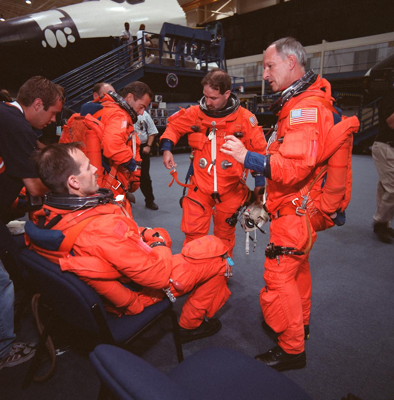 S99-08668 --- Four members of the STS-103 crew prepare their launch and entry suits for a training session  on emergency bailout procedures in the Johnson Space Center's Systems Integration Facility. Astronaut Steven L. Smith is seated in the foreground.  Others pictured are astronauts  Jean-Francois Clervoy, John M. Grunsfeld and Claude Nicollier, all mission specialists.  Nicollier and Clervoy are with the European Space Agency (ESA).  One of two Crew Compartment Trainers (CCT) is in the background.