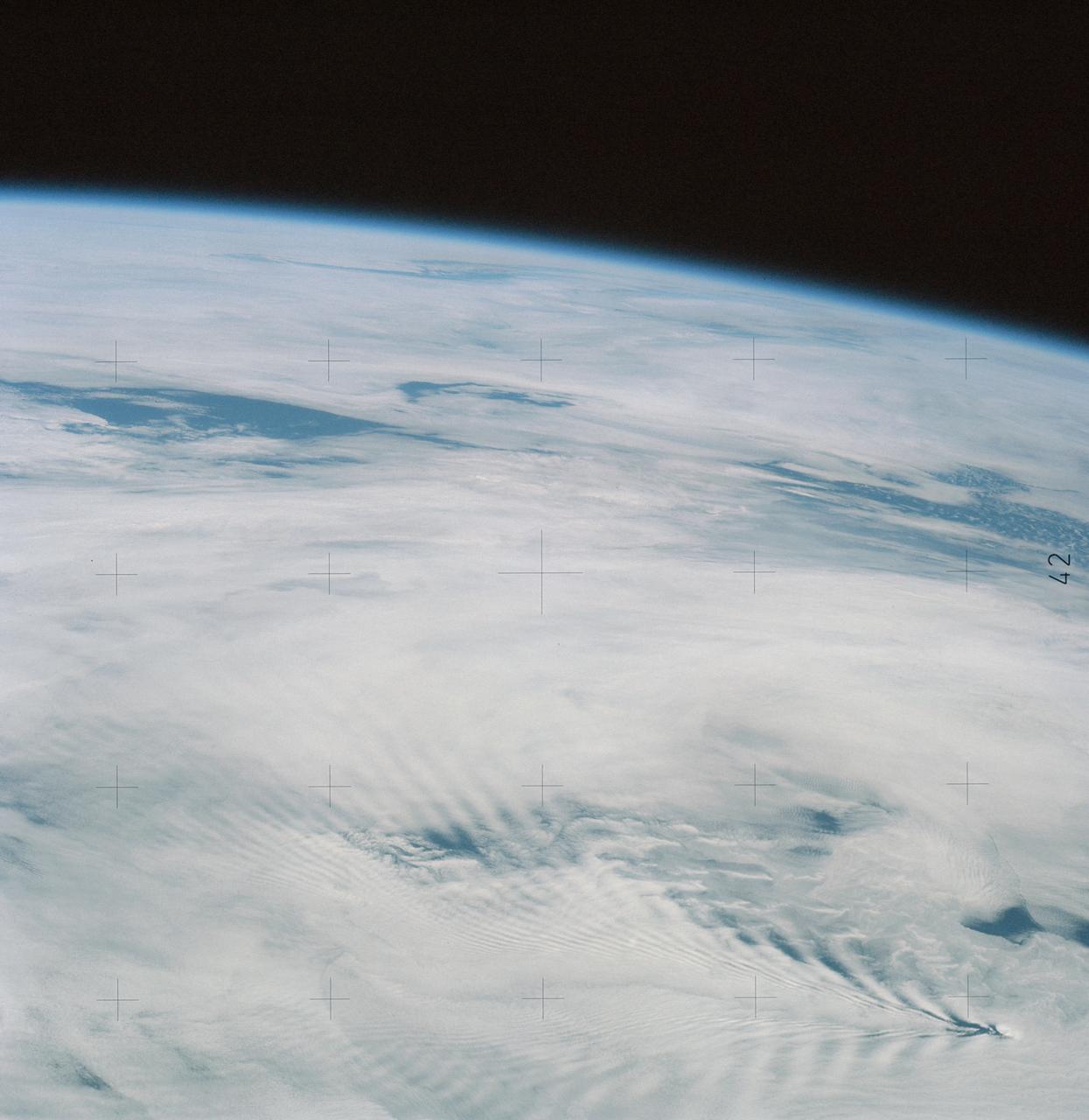 SL4-137-3632 (February 1974) --- A photograph taken from the Skylab space station in Earth orbit illustrating an atmospheric wave pattern by the affect of a small mountainous island on wind currents. Various patterns can be seen downwind of small islands. Often a Von Karmon vortex can be seen which appears as a spiral pattern. Multiple vortices have been photographed on previous missions. This photograph illustrates a "bow wave" pattern which extends for hundreds of miles downwind from the island. The island itself is often clear when a wave pattern is formed downstream. This particular pattern is very symmetrical. These wave patterns are most common in the South Pacific. This picture was taken by a Skylab 4 crewmen using a hand-held 70mm Hasselblad camera. Photo credit: NASA