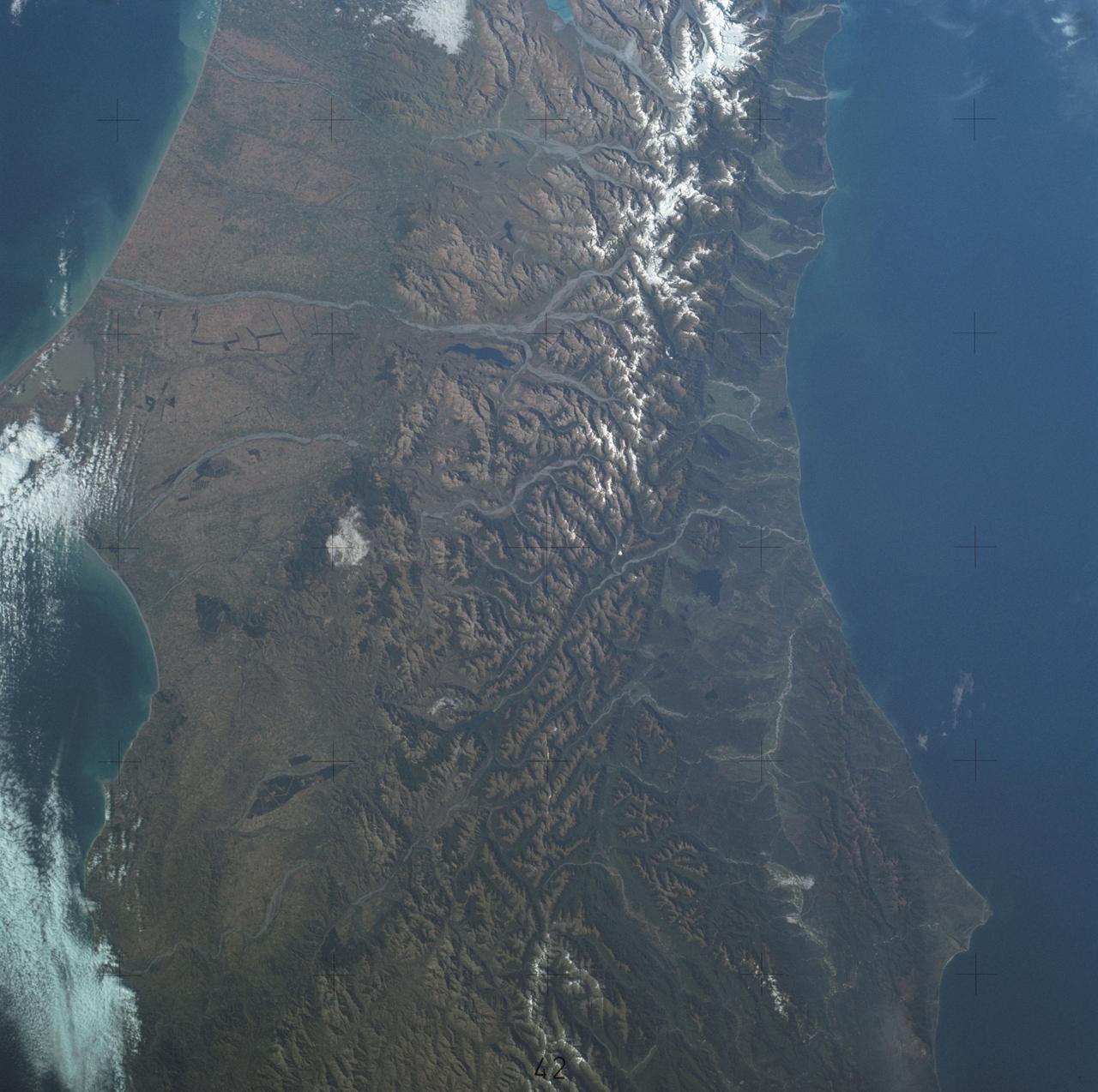 SL4-137-3700 (22 Dec. 1973) --- A near vertical view of a portion of South Island, New Zealand, as see from the Skylab space station in Earth orbit. This picture was taken by one of the Skylab 4 crew members with a handheld 70mm Hasselblad camera using a 100mm lens. The picture should be held with the largest body of water (Tasman Sea) on the left. Cape Foulwind is at the upper left. The City of Christchurch is under clouds at the center right margin. Note the movement of sediment by alongshore currents, especially on the east (right) side of the island. The Alpine Fault, which is part of the circum-Pacific volcanic-tectonic belt, is clearly visible on the left (west) side of the island. The fault line is marked by a scarp, which appears very distinct from orbital altitude. Differences in topography and vegetation on either side of the fault are also sharp. Streams change direction at the fault line, and the change in slope at the fault line is evident in the widening of stream channels. The left side of the fault has moved northeast (upward) relative to the right side; some stream offsets indicate the direction of relative movement, but others are controlled by local topography. The Alpine Fault, which also transects New Zealand's North Island, was photographed and described more than a dozen times by the Skylab 4 crewmen. The circum-Pacific volcanic-tectonic belt is a feature of the Earth's crust which is related to sea floor spreading and continental drift. Though the Alpine Fault is sharply delineated in this photograph, other major crustal features are subtle that their existence was unknown before their observation from orbit. The distance from top to bottom is about 290 kilometers (175 miles). Photo credit: NASA