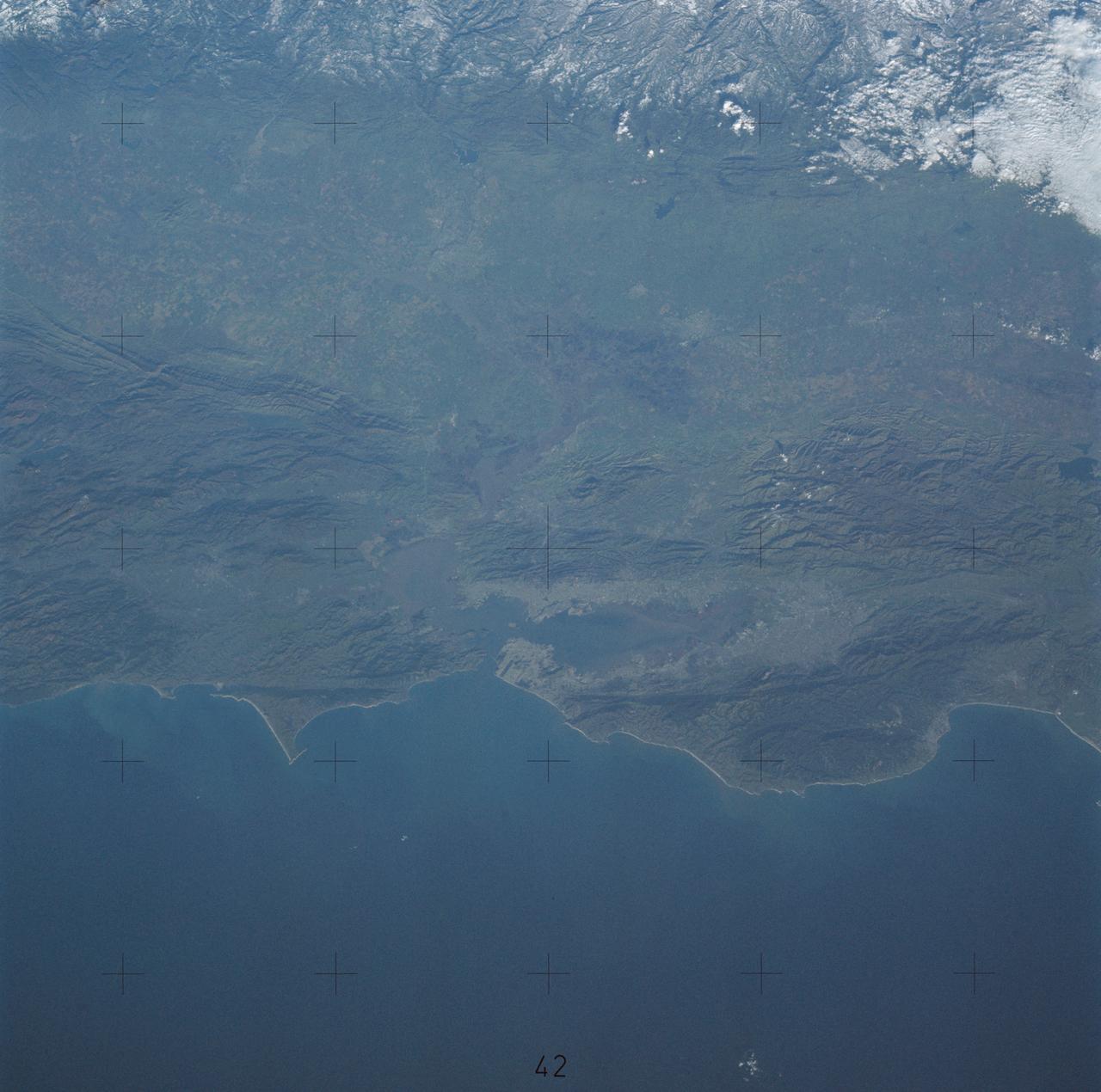 SL4-138-3843 (1 Jan. 1974) --- A part of northern California centered near San Francisco Bay photographed at 3 p.m. Jan. 2, 1974, from the Skylab space station in Earth orbit. This near vertical view encompasses the coastline from Monterey Bay (right) to about 50 miles north of Point Reyes (left) and includes, from bottom to top, San Francisco Bay (center), Sacramento Valley (left center), San Joaquin Valley (right center), and the snow-covered Sierra Nevada. Afternoon shadows sharply delineate a valley which parallels San Francisco Bay, crosses Point Reyes, and lies between the Bay and the Pacific coastline. This valley marks the location of the San Andreas Fault, a major break in the Earth's crust. Forces acting on the crust are causing the land west (bottom) of the fault line to move north relative to land on the east side. The Skylab 4 astronauts photographed major fault zones in South America, New Zealand, Japan and Africa for use in the study of worldwide tectonic system. Agricultural areas in the Sacramento and San Joaquin Valleys are indicated by the tan areas which are easily discerned in contrast to the green-gray background. Photo credit: NASA