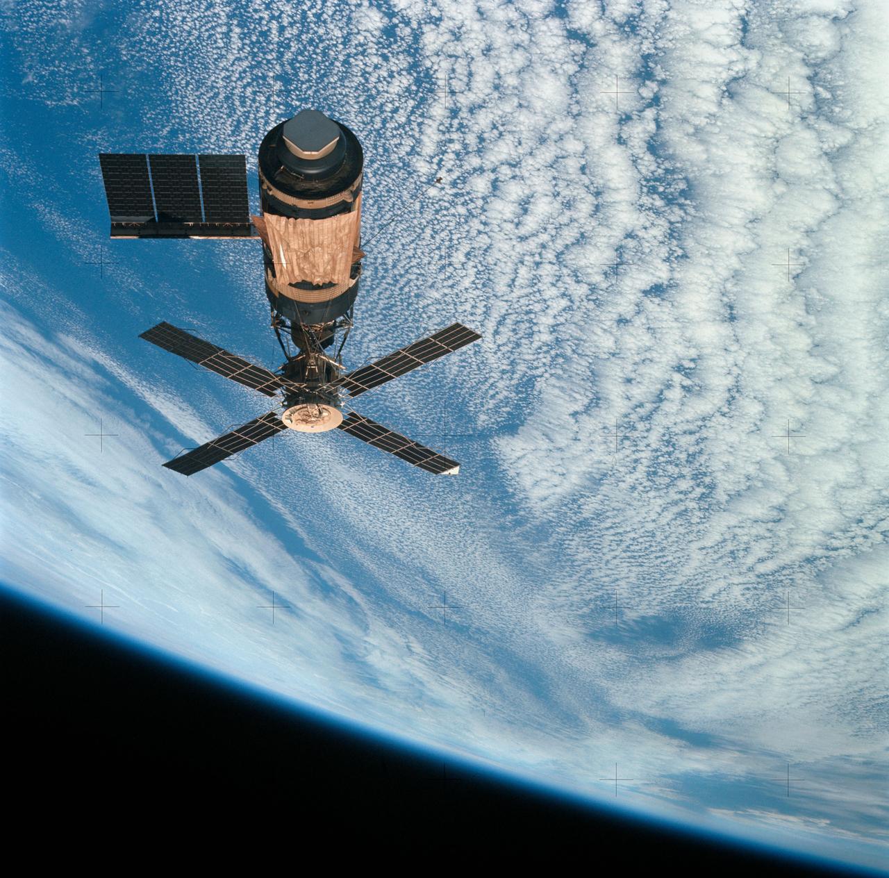 SL4-143-4707 (8 Feb. 1974) --- An overhead view of the Skylab space station cluster in Earth orbit as photographed from the Skylab 4 Command and Service Modules (CSM) during the final fly-around by the CSM before returning home. The space station is contrasted against a cloud-covered Earth. Note the solar shield which was deployed by the second crew of Skylab and from which a micrometeoroid shield has been missing since the cluster was launched on May 14, 1973. The OWS solar panel on the left side was also lost on workshop launch day. Photo credit: NASA