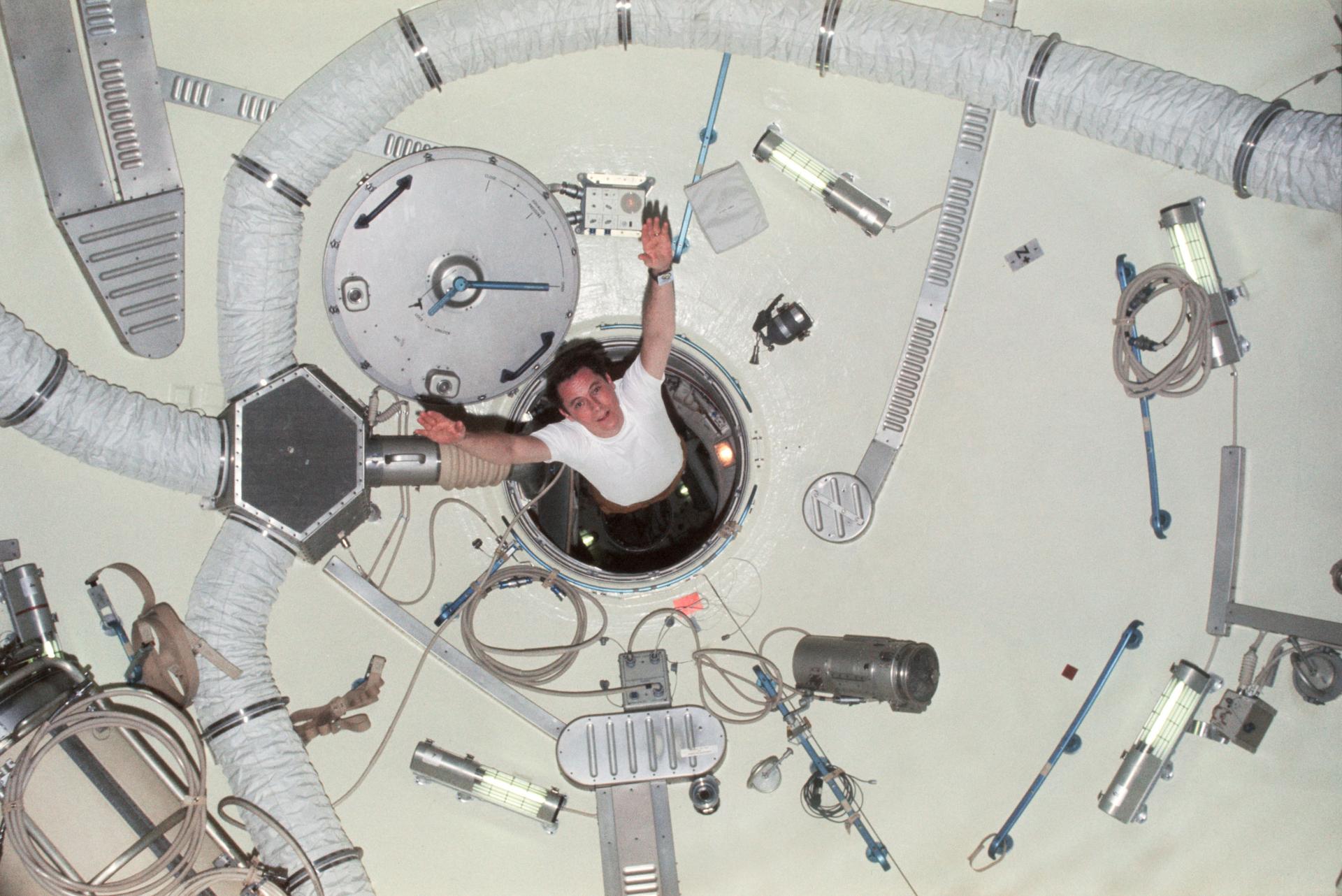 Skylab 4 astronaut floats through Skylab's airlock module hatch with his arms outstretched.