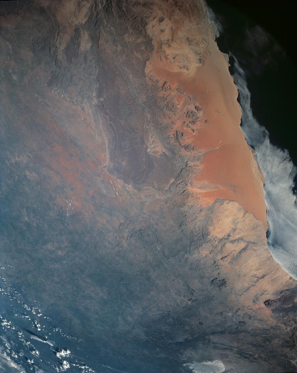 One of the driest regions on Earth, the Namib Desert, Namibia, Africa (23.0N, 15.0E) lies adjacent to the Atlantic coast but the upwelling oceanic water causes a very stable rainless atmosphere. The few local inland rivers do not reach the sea but instead, appear as long indentations where they penetrate the dune fields and end as small dry lakes. The vast dune fields are the result of sands deposited over millions of years by the stream flow.