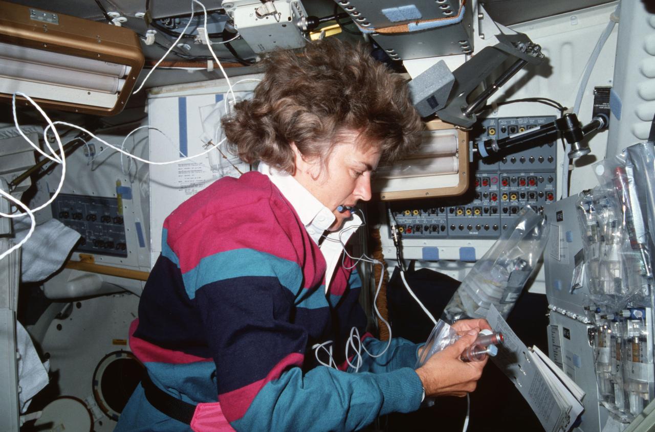 STS043-03-001 (2-11 Aug 1991) --- Astronaut Shannon W. Lucid, STS-43 mission specialist, is pictured with a sample from the Bio-serve Instrumentation Technology Associates Materials Dispersion Apparatus (BIMDA).  BIMDA is designed to obtain data on scientific methods and commercial potential for growing large high quality protein crystals in microgravity. The experimental focus is on both synthetic and natural biological processes that provide the foundation of the assembly of large structures from macromolecules.  In addition, cell processes and membrane (cell and artificial) processes are being evaluated.  BIMDA experiments are stored and operated on the middeck in a refrigerator/incubator module (R/IM).  During this flight, the R/IM maintains a constant internal temperature of 20 degrees Celsius.  This experiment also flew on NASA?s STS-37 mission.