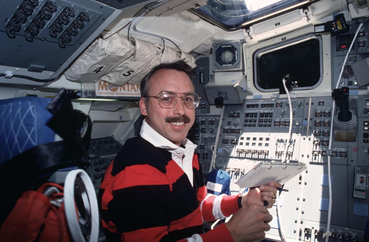 STS043-04-038 (2-11 Aug 1991) --- Astronaut James C.  Adamson, STS-43 mission specialist, checks on an experiment on Atlantis? flight deck.  Part of the experiment, Optical Communications Through the Shuttle Window (OCTW), can be seen mounted in upper right.  The OCTW system consists of two modules, one inside the orbiter crew cabin (as pictured here) and one in the payload bay. The crew compartment version houses an optoelectronic transmitter/receiver pair for video and digital  subsystems, test circuitry and interface circuitry. The payload bay module serves as a repeater station.  During operation a signal is transmitted through the shuttle window to a bundle of optical fiber cables mounted in the payload bay near an aft window. The cables carry optical signals from the crew compartment equipment to the OCTW payload bay module.  The signals are returned via optical fiber cable to the aft flight deck window, retransmitted through the window, and received by the crew compartment equipment.