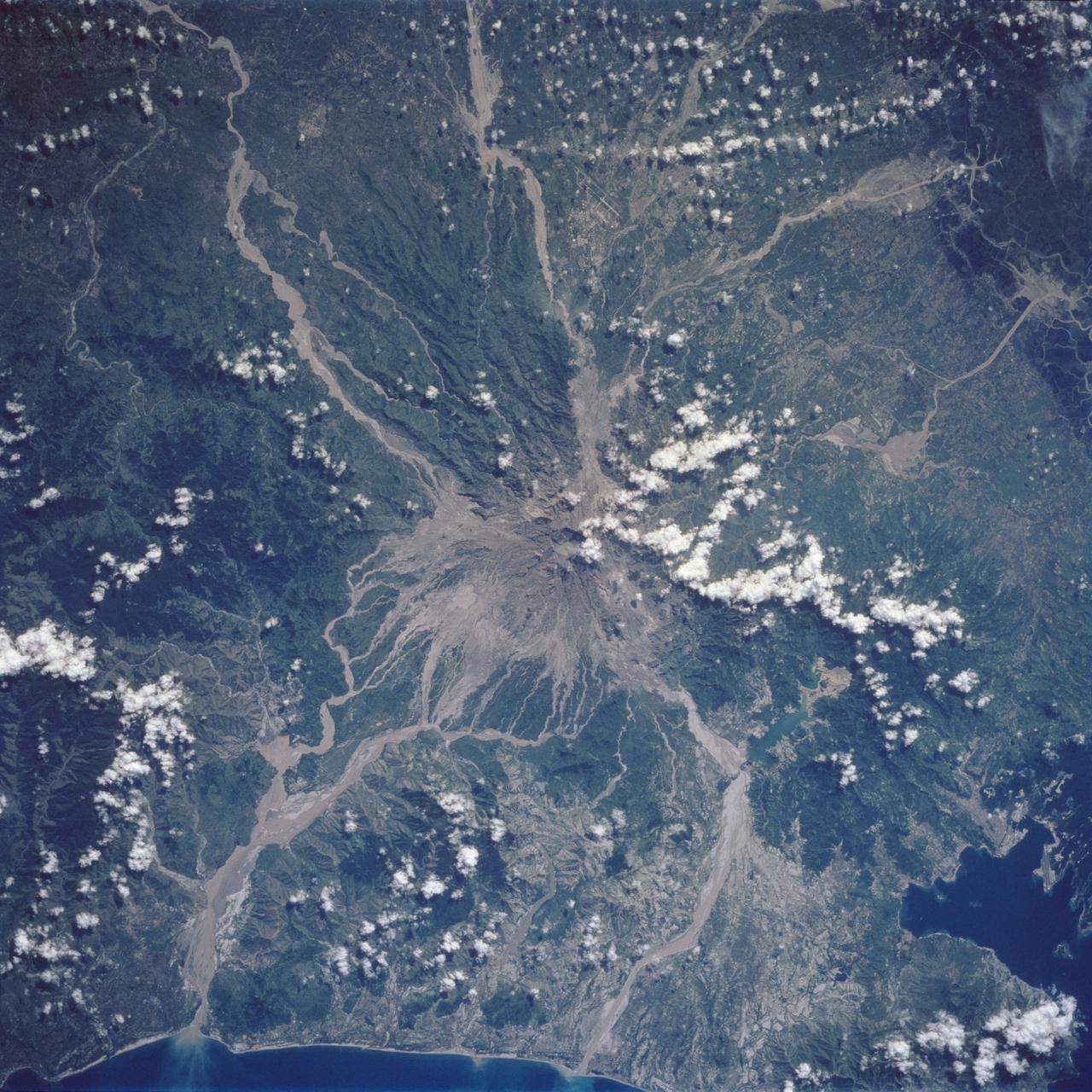 Mt. Pinatubo on the island of Luzon (15.0N, 120.0E) erupted catastrophically in June 1991 after over 600 years of inactivity. In this vertical view, the full extent of the eruption is obvious. Thick layers of ash completely surrounds the crater and the effect of mudflows in this previously heavily forested and agricultural region can be traced as ribbons flowing downhill. Clark AFB, once the crossroads of the SW Pacific can only partially be seen.