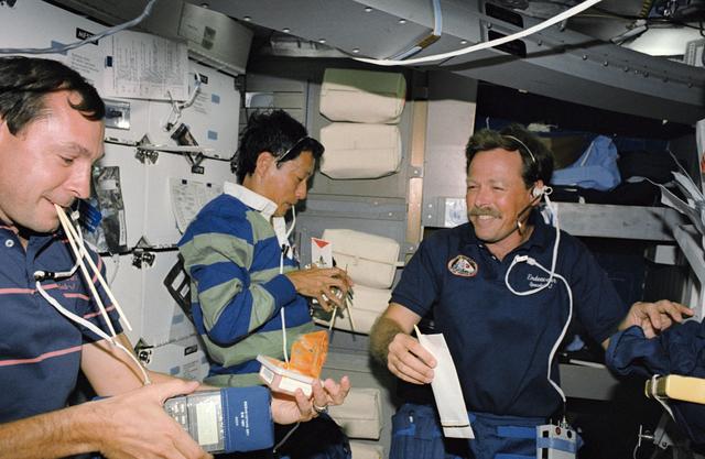 NASA image: STS-47 crewmembers eat on OV-105's middeck using chopsticks