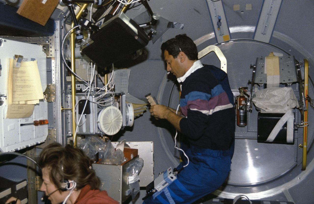 STS050-254-007 (25 June-9 July 1992) --- Lawrence J. DeLucas, payload specialist, handles a Protein Crystal Growth (PCG) sample at the multipurpose glovebox aboard the Earth-orbiting Space Shuttle Columbia.  Astronaut Bonnie J. Dunbar, payload commander, communicates with ground controllers about the Solid Surface Combustion Experiment (SSCE), one of the United States Microgravity Laboratory 1’s (USML-1) three experiments on Rack 10.  Five other crew members joined the pair for a record-setting 14-days of scientific data gathering.