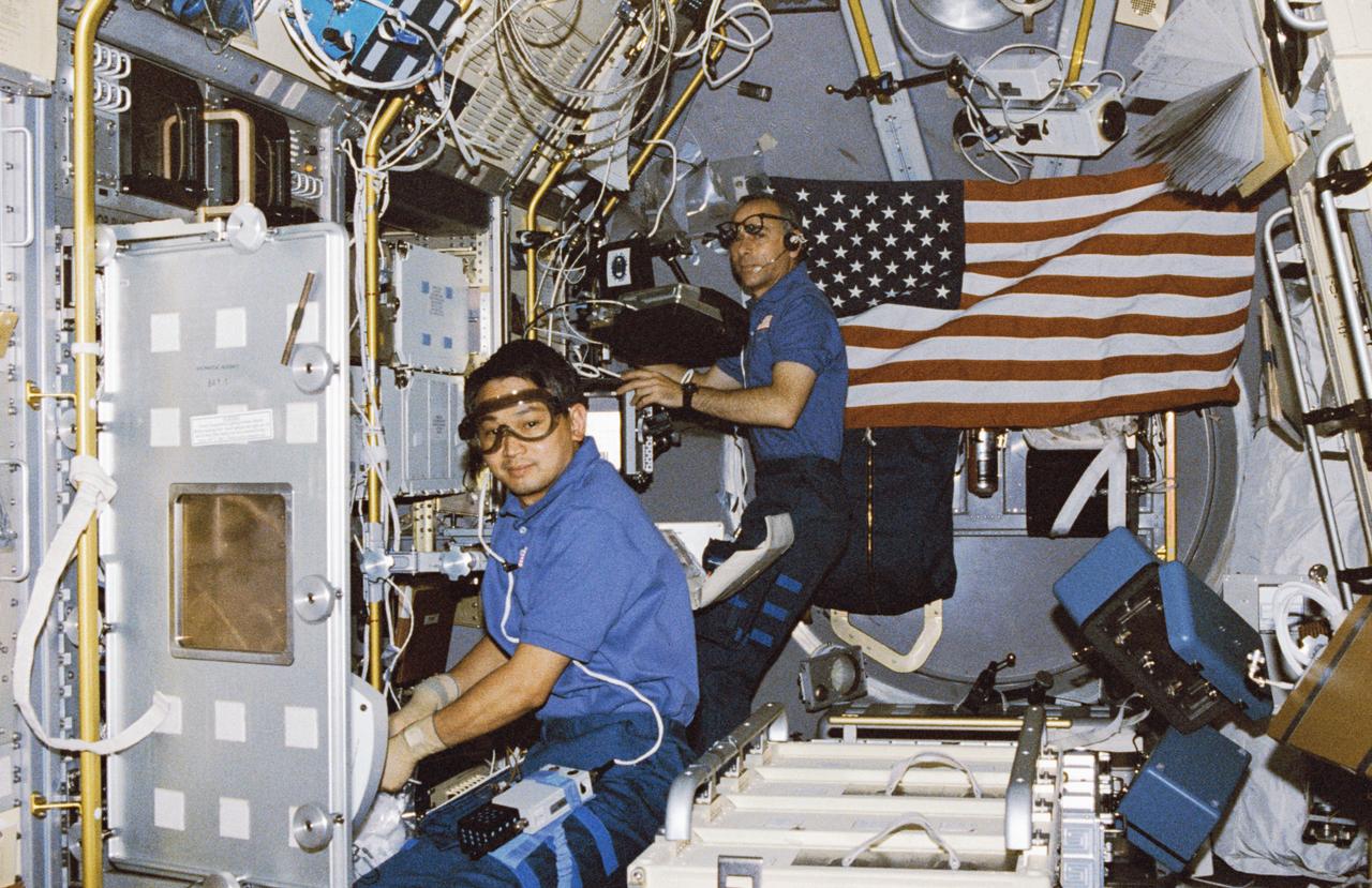 STS050-255-027 (25 June-9 July 1992) --- Payload specialist Eugene H. Trinh, left, and astronaut Carl J. Meade, mission specialist, go to work in the U.S. Microgravity Laboratory (USML-1) science module as the blue shift crew takes over from the red.  Trinh is working with an experiment at the Drop Physics Module (DPM) and Meade prepares to monitor an experiment in the Glovebox.  The two joined four other astronauts and a second scientist from the private sector for 14-days of scientific data-gathering.