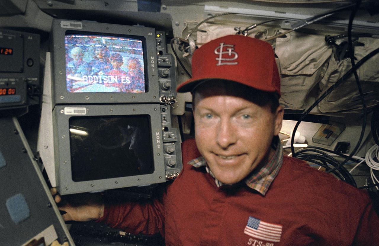 STS50-39-006 (25 June-9 July 1992) --- Astronaut Richard N. Richards, STS-50 mission commander, stands by a monitor displaying a group of elementary pupils (Addison Elementary School, Marietta Georgia) who were among the many students and others on Earth who communicated with members aboard the Earth-orbiting Space Shuttle Columbia.  The Shuttle Amateur Radio Experiment (SAREX) has flown on a number of STS missions now, allowing hundreds of students and "hams" the chance to communicate with licensed radio operators in space.  Richards is KB5SIW and astronaut Ellen S. Baker, the crew's other licensed operator, is KB5SIX.