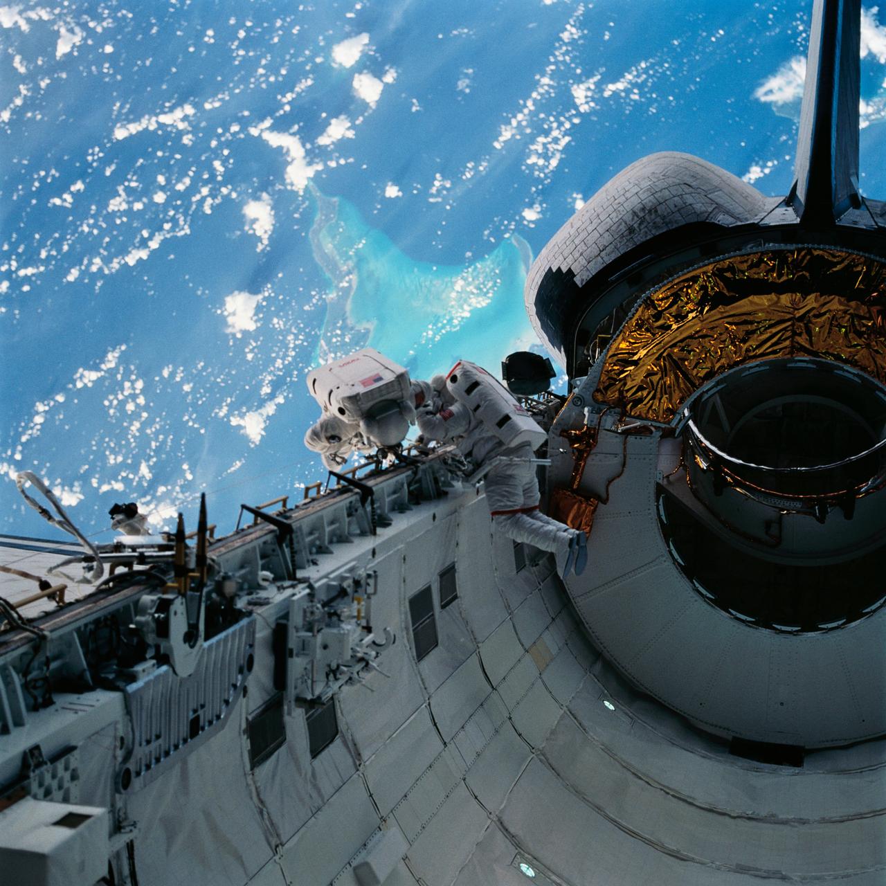 With the Caribbean Sea and part of the Bahama Islands chain as a backdrop, two STS-51 crewmembers evaluate procedures and gear to be used on the upcoming Hubble Space Telescope (HST)-servicing mission. Sharing the lengthy extravehicular activity in and around Discovery's cargo bay were astronauts James H. Newman (left), and Carl E. Walz, mission specialists.