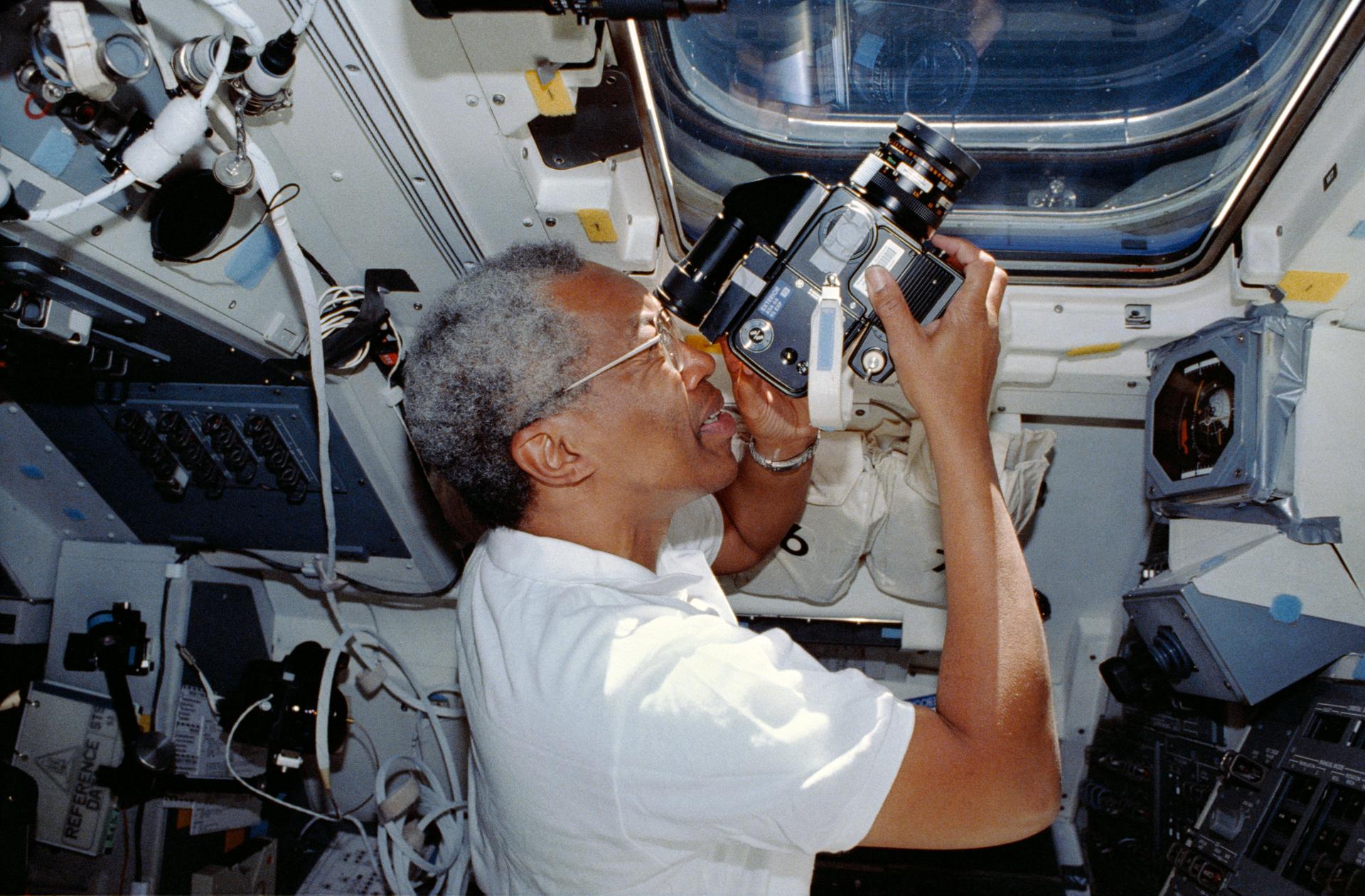 Guy Bluford holds a camera to capture a scene outside the Space Shuttle window