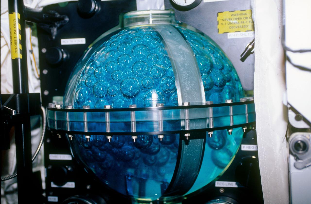 STS053-09-019 (2 - 9 Dec 1992) --- A medium close-up view of part of the Fluid Acquisition and Resupply Equipment (FARE) onboard the Space Shuttle Discovery.  Featured in the mid-deck FARE setup is fluid activity in one of two 12.5-inch spherical tanks made of transparent acrylic.  Pictured is the receiver tank.  The other tank, out of frame below, is for supplying fluids.  The purpose of FARE is to investigate the dynamics of fluid transfer in microgravity and develop methods for transferring vapor-free propellants and other liquids that must be replenished in long-term space systems like satellites, Extended-Duration Orbiters (EDO), and Space Station Freedom.  Eight times over an eight-hour test period, the mission specialists conducted the FARE experiment.  A sequence of manual valve operations caused pressurized air from the bottles to force fluids from the supply tank to the receiver tank and back again to the supply tank.  Baffles in the receiver tank controlled fluid motion during transfer, a fine-mesh screen filtered vapor from the fluid, and the overboard vent removed vapor from the receiver tank as the liquid rose.  FARE is managed by NASA's Marshall Space Flight Center (MSFC) in Alabama.  The basic equipment was developed by Martin Marietta for the Storable Fluid Management Demonstration.  Susan L. Driscoll is the principal investigator.