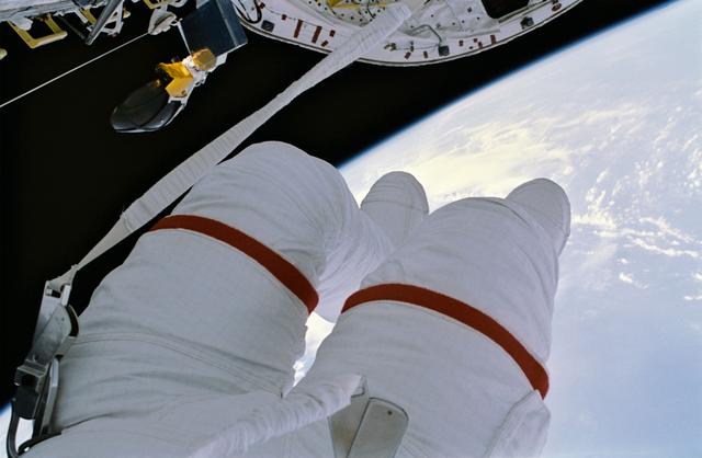 NASA image: EVA crewmember's legs dangling over empty space and payload bay.