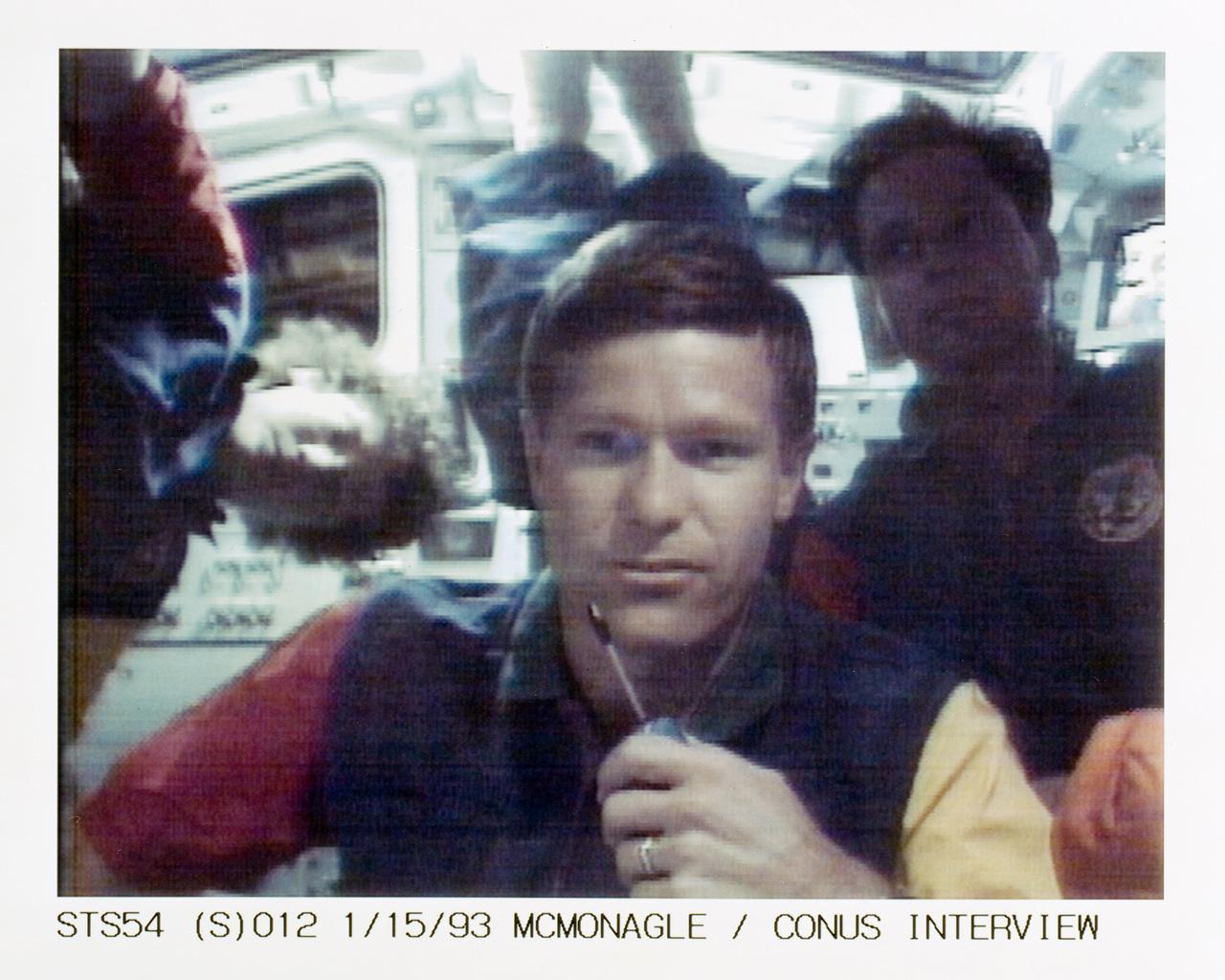 STS054-S-012 (15 Jan 1993) --- McMonagle talks to a radio station from the flight deck of Endeavour while, in the background, several crewmates await their turns to communicate with other stations. The scene was recorded at 13:54:14:13 GMT, Jan. 15, 1993.