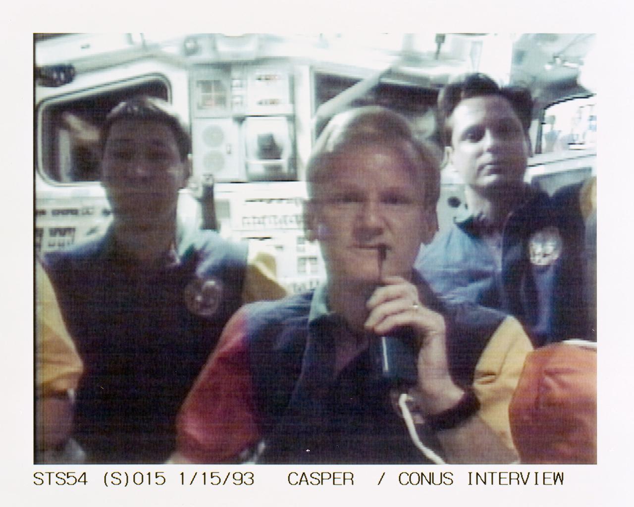 STS054-S-015 (15 Jan 1993) --- Casper talks to a radio station from the flight deck of Endeavour while, in the background, Runco, left, and Harbaugh await their turns to communicate with other stations. The scene was recorded at 13:45:54:05 GMT, Jan. 15, 1993.