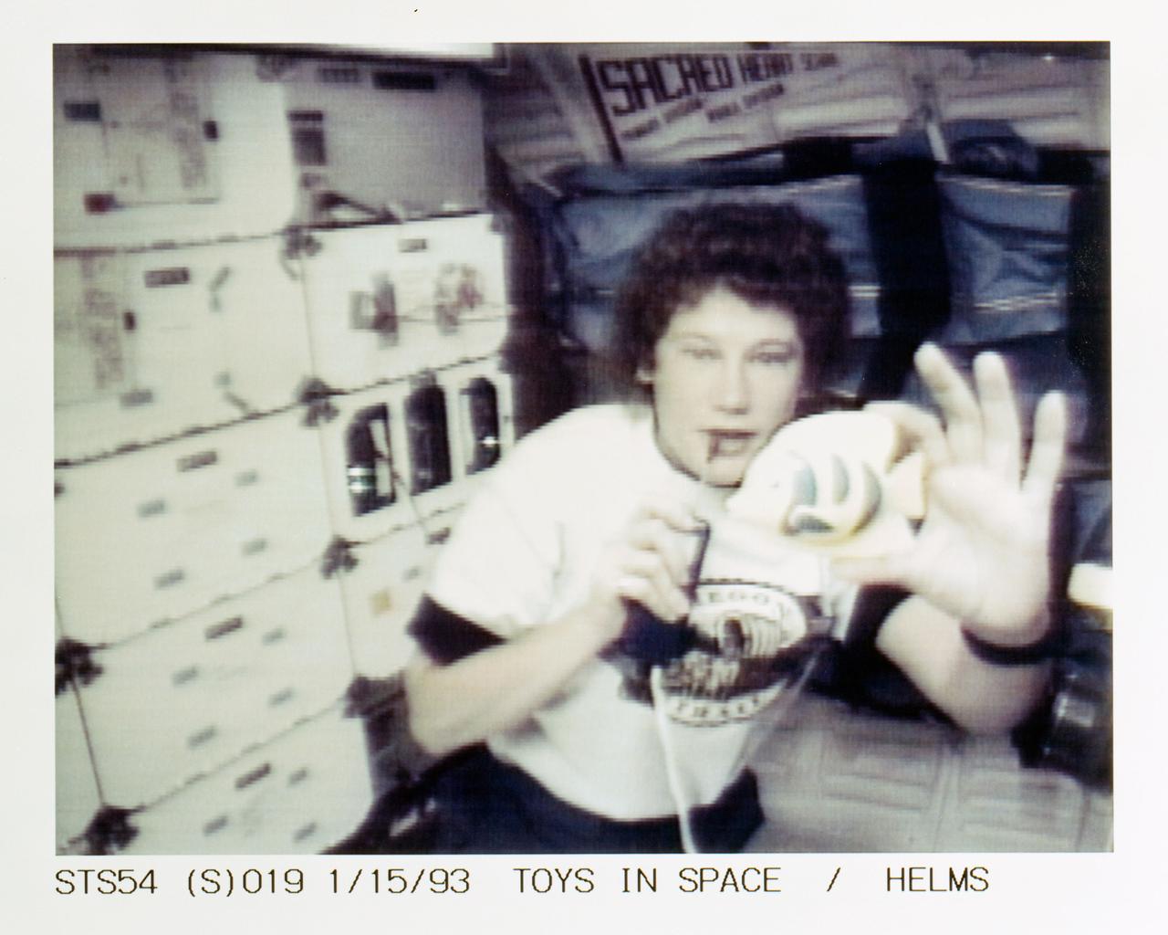 STS054-S-019 (15 Jan 1993) --- Helms with a fish toy on the middeck demonstrates some of the physics of toys to students watching on television. Four schools were chosen to ask questions of the astronauts during the lengthy program. Helms fielded questions from students at Shaver Elementary School in Portland, Oregon. The fish was used to demonstrate Newton's third law of motion and the conservation of angular momentum. The entire collection of toys will be videotaped for an educational program to be distributed to schools in the fall of this year. The scene was recorded at 17:50:08:27 GMT, Jan. 15, 1993.