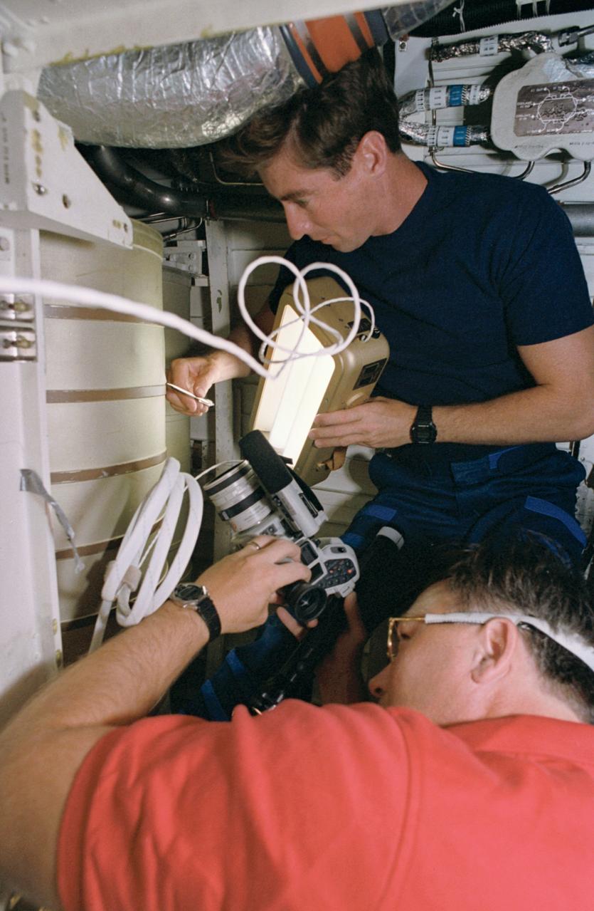 STS055-39-036 (26 April-6 May 1993) --- Astronaut Terence T. (Tom) Henricks, pilot, uses a spotlight and pen to point out a possible problem area on a waste water tank in the bilge area below Columbia's middeck. Astronaut Jerry L. Ross, payload commander, records the activity with a camera.