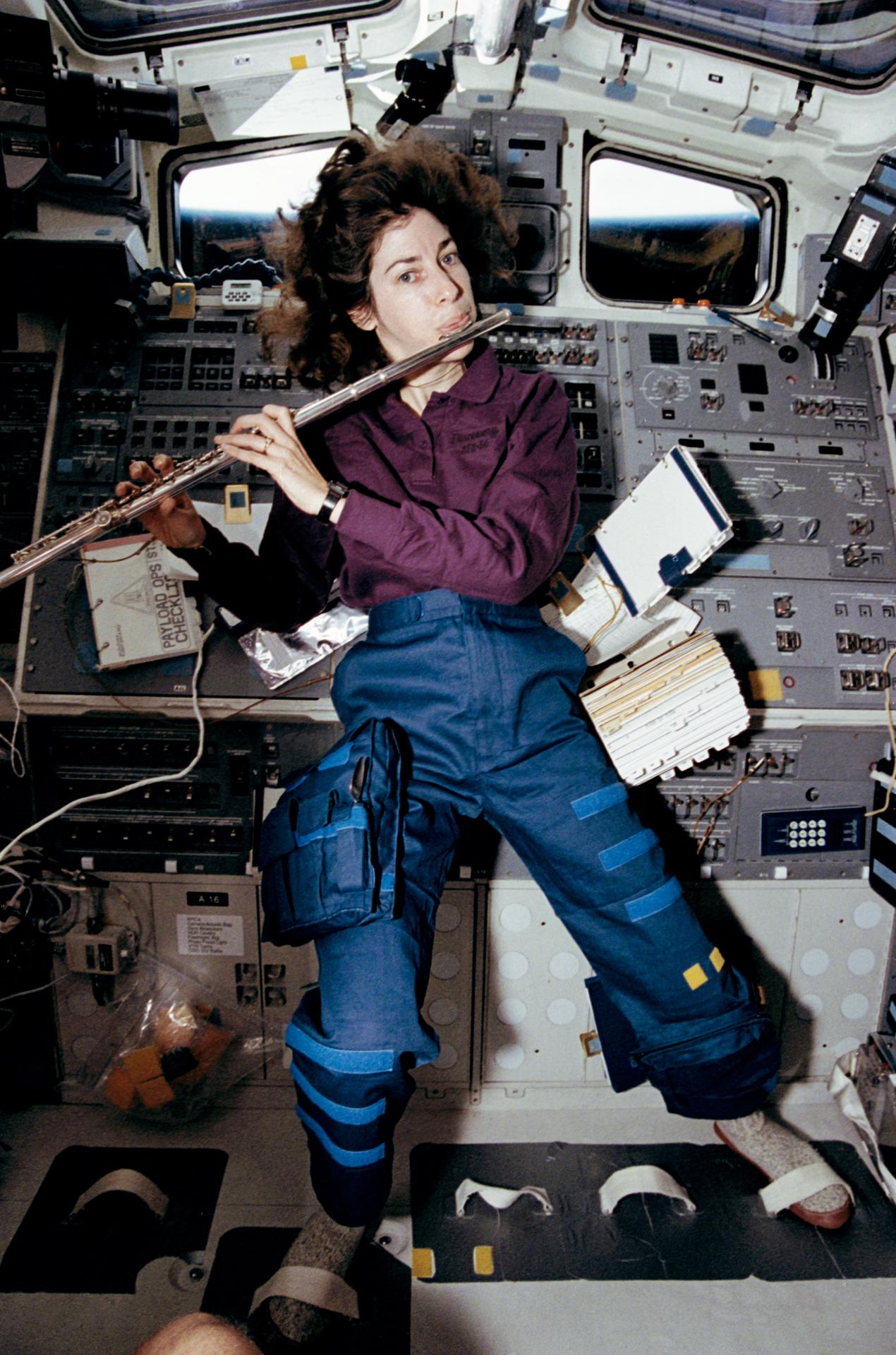 Ellen Ochoa playing a flute while floating on Discovery's aft flight deck.