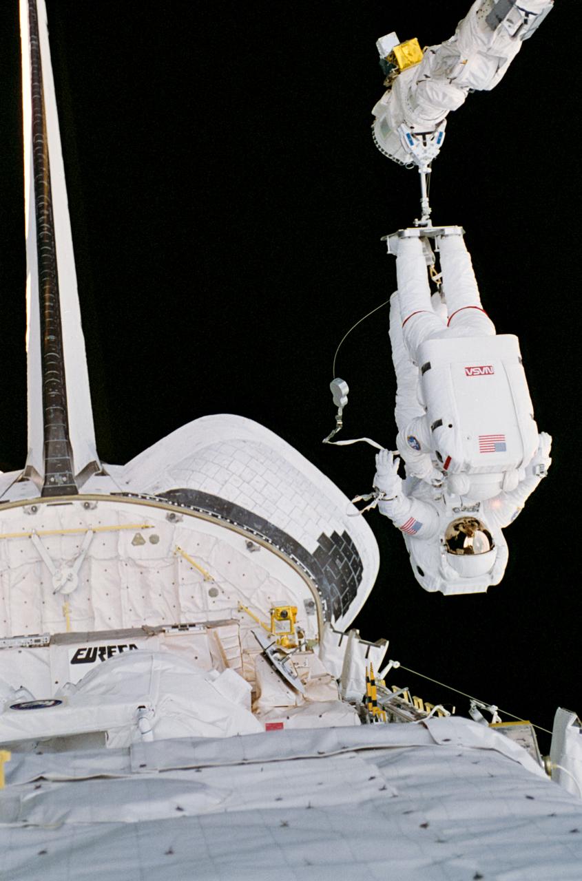 STS057-32-008 (25 June 1993) --- Astronaut G. David Low (nearer camera), his feet anchored to Endeavour's Remote Manipulator System (RMS), lifts fellow astronaut Peter J. K. (Jeff) Wisoff during a special phase of the lengthy June 25, 1993, extravehicular activity (EVA).  This phase of the EVA dealt with the simulation of handling large components in space.  This particular task was rehearsed with eyes toward the servicing of the Hubble Space Telescope (HST) in the near future or the assembly and maintenance of the International Space Station later.  The two mission specialists and four other NASA astronauts spent almost ten days aboard the Space Shuttle Endeavour in Earth-orbit supporting the SPACEHAB mission, retrieving the European Retrievable Carrier (EURECA) and conducting various experiments.