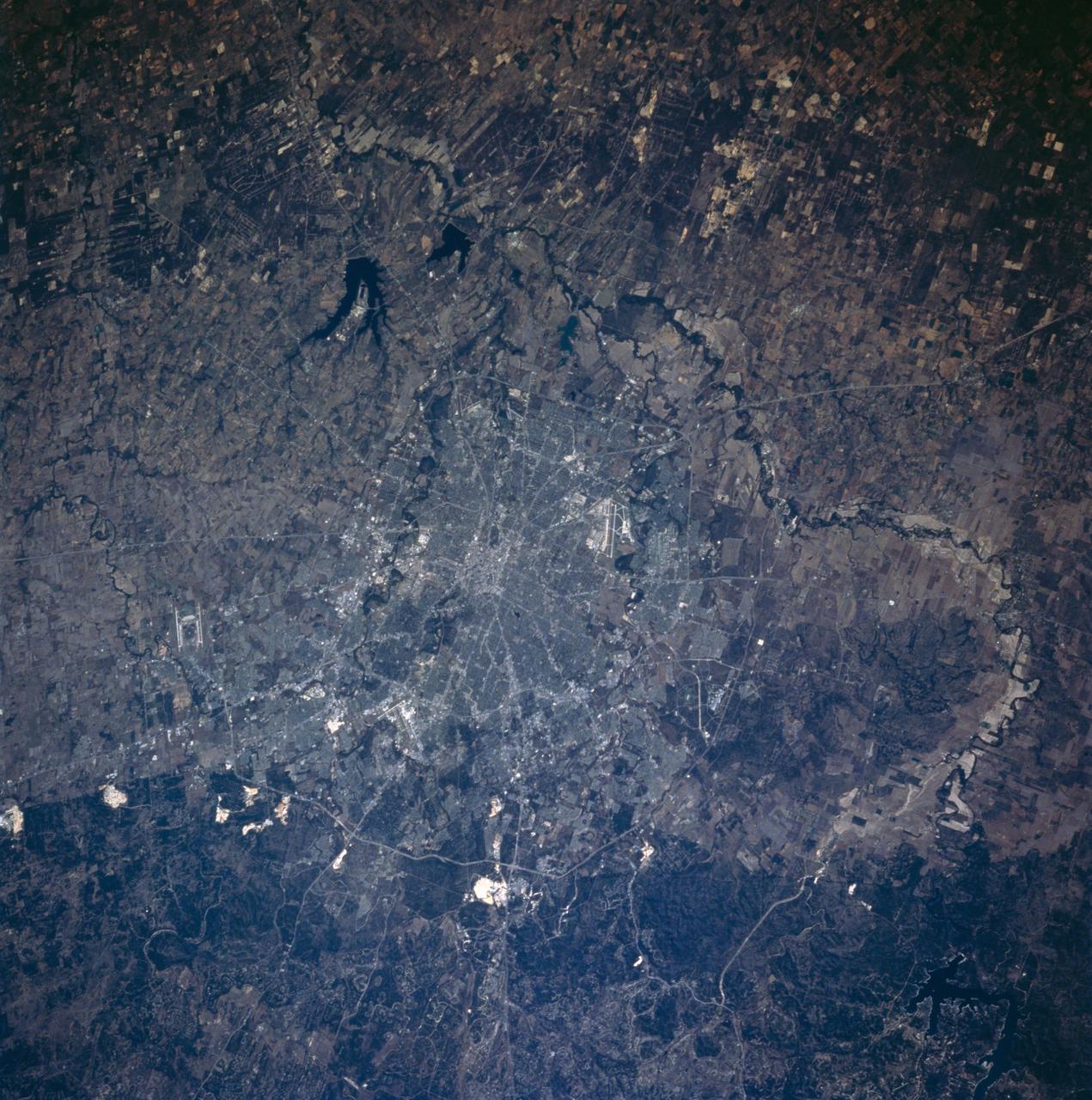 STS058-101-053 (18 Oct-1 Nov 1993) --- This sharp cloud-free photograph of San Antonio, Texas illustrates the classic pattern of western cities.  The Hispanic heart of the city; an intertwining of streets along the San Antonio River and around the Alamo, surrounded by a late 19th century Anglo grid of small businesses and suburban homes.  Transportation routes radiate to mid and late 20th Century ring corridors separating the urban/suburban region from the surrounding agricultural countryside.  San Antonio was founded around permanent springs that rise at the foot of the Balcones Escarpment, which separates the Texas Hill Country from the South Texas Plains.  Limestone quarries are conspicuous along the edge of the escarpment.  San Antonio has long been a major site for military training bases: Randolph Air Force Base is outside the city to the northeast, Fort Sam Houston is contained within the northeast quadrant of the city, Brooks Air Force Base lies at the southeastern corner, and Lackland and Kelly Air Force Bases are within the suburban fringe to the southwest.  San Antonio International Airport can be seen at the foot of the escarpment in the northern part of the city.