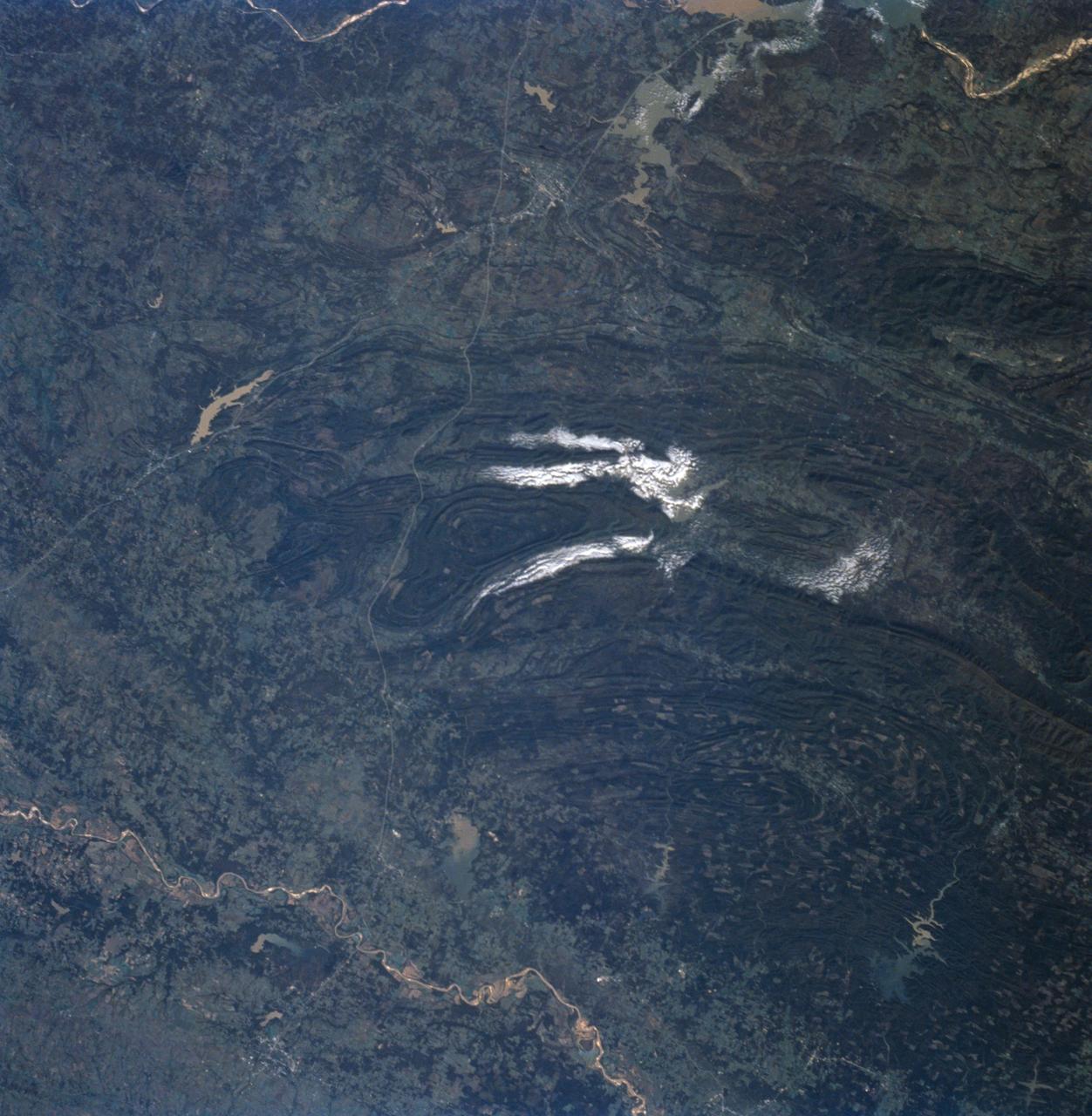 STS058-91-058 (18 Oct-1 Nov 1993) --- In this unusually clear view, the Ouachita Mountains of southeastern Oklahoma are framed on the north by Lake Eufaula on the South Canadian River, and on the south by the Red River.  Sandstone, shale and chert (similar to flint) deposited in a sea several thousand feet deep were squeezed up to form the mountains about 250 million years ago.  During the ensuing time, erosion of the western end of the Ouachita Mountains has emphasized linear ridges of resistant rock in the plunging anticlines and synclines, causing relief of 800 meters (2,600 feet) or more.  Clouds formed by upslope winds border both the north and south sides of one of the most dramatic plunging synclines (in a syncline the rock layers dip toward the center of the structure).  Toward the west, densely forested mountains give way to gently rolling, less rocky terrain and a drier climate which is better suited to farming.  The mountains centered on Broken Bow, in the lower right corner of the scene, display abundant timber clearcuts that are being regenerated.