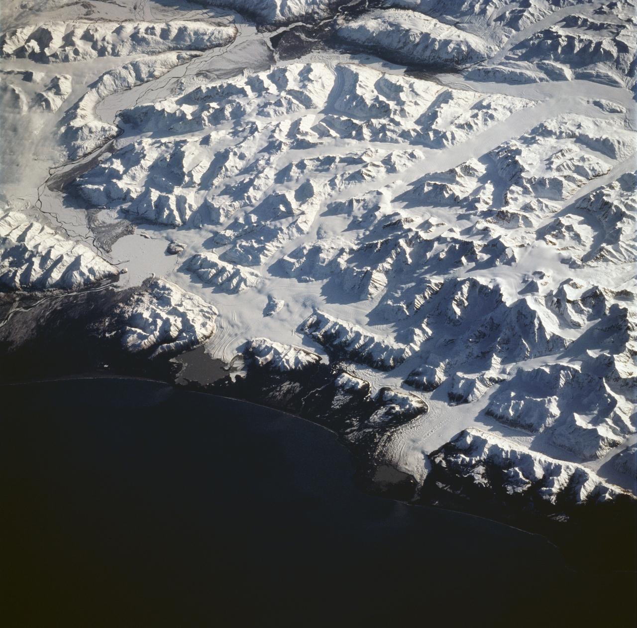 STS059-228-094 (9-20 April 1994) --- The spring thaw along the coast of the Gulf of Alaska has not touched the St. Elias Mountains, southeast of Yakutat Bay and Malaspina Glacier.  A prominent glacier flows from Mt. Fairweather (15,300 feet) at right center, to form Cape Fairweather.  Another glacier to the northwest almost reaches the sea; the valley of the Alsek River forms a broad, braided plan at upper left.  The low sun elevation and oblique angle of this photograph provide a striking 3-dimensional appearance to the black-and-white landscape.  SRL investigators will study microwave response to varying depths and conditions of ice and snow along this coast, in Spring and Summer.  Hasselblad photograph.