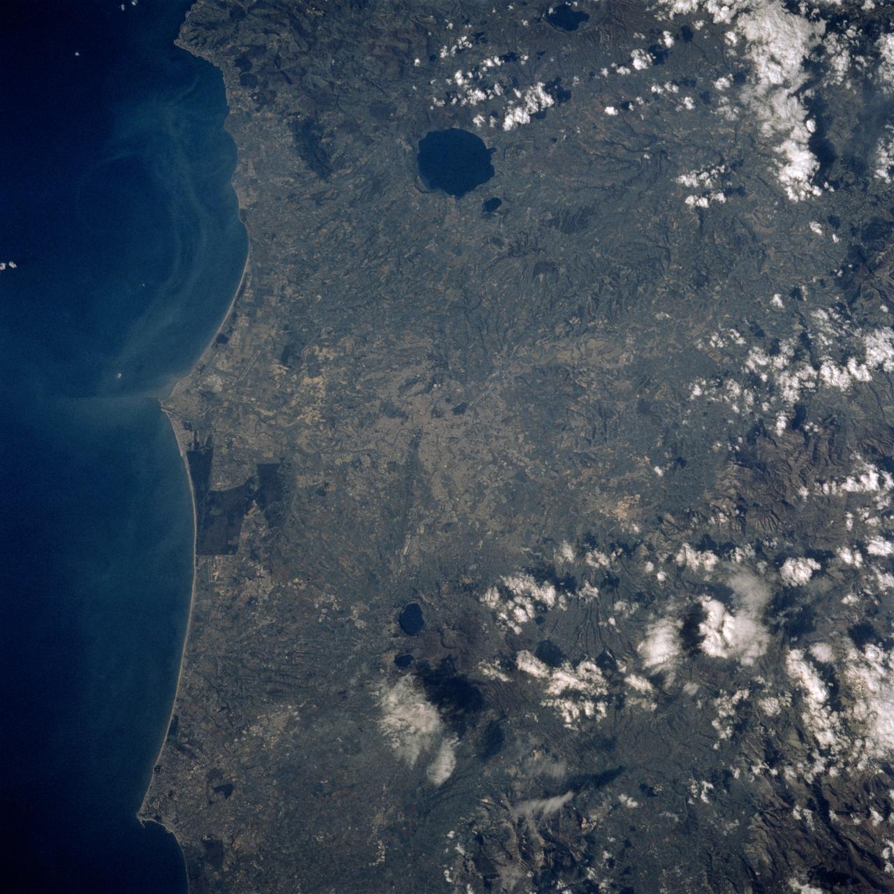 STS060-90-028 (3-11 Feb 1994) --- This view is centered over Rome and covers approximately 3,600 square miles.  Anzio, the site of the January 22, 1944, Allied landing in Central Italy, is on the coast at the lower left.  The coastal protuberance near the center is Ostia.  This Roman Empire port on the Tiber River silted in and was covered over.  It is now an archeological site and a tourist attraction.  Southeast of the mouth of the Tiber is the Pontine Marsh.  These marshlands were drained in the 1930's and have been converted to farmland.  Volcanism formed the land in the region.  It is evidenced in the circular caldera lakes visible.  Castel Gandolfo, part of the Papal State, is on Lake Albano toward the bottom of the frame.  Rome was founded during the Bronze Age on a river crossing.  The road from the coast along the river was the main route for the early salt trade.  The city became the capital of modern Italy in 1861.  It has undergone explosive growth since World War II and now has a population of over three million people.  Leonardo da Vinci (Fiumicino) Airport, the main international airport, is visible near the coast north of the Tiber River.