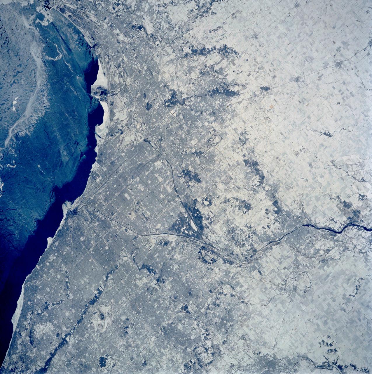 STS060-103-089 (3-11 Feb. 1994) --- The Chicago, Illinois area is in this northeast looking low oblique view obtained in February, 1994. Lake Michigan, a good portion covered with ice due to the very cold winter weather that has plagued this region since early December, 1993, can be seen to the east of the city. The Des Plaines river is visible traversing northeast to southwest through the center of the city. O'Hare International Airport and the Glenview Naval Air Station can be seen to the north of the Des Plaines River. Midway Airport is visible just to the south of the river. Chicago is a port of entry; a major Great Lakes port located at the junction of the St. Lawrence Seaway with the Mississippi River system; the busiest air center in the United States; and an important rail and highway transportation hub. Chicago is known for large grain mills and elevators, iron and steel works, steel fabrication plants, stockyards, meat-packing establishments, and printing and publishing houses. In the early days of settlement, the narrow watershed between Lake Michigan and the Des Plaines River (draining the Mississippi River through the Illinois River), offered an easy portage that led explorers like Father Marquette and Louis Joliet and others to the Great Central Plains. Fort Dearborn, a military post was established in 1803. By 1860, the railroad connected Chicago to the rest of the country and the city became a great mid-continent shipping and receiving center. In 1871, the city built of wood, was almost entirely destroyed by a great fire. After the fire, Chicago was built as a city of steel and stone. During the World's Colombian Exposition held in Chicago in 1893, the city became a leading architectural center. It was here during the Exposition that the skyscraper came into being. Chicago continues to lead the way in this type of architectural structure as is evidenced with the completion of the Sears Tower in 1974.