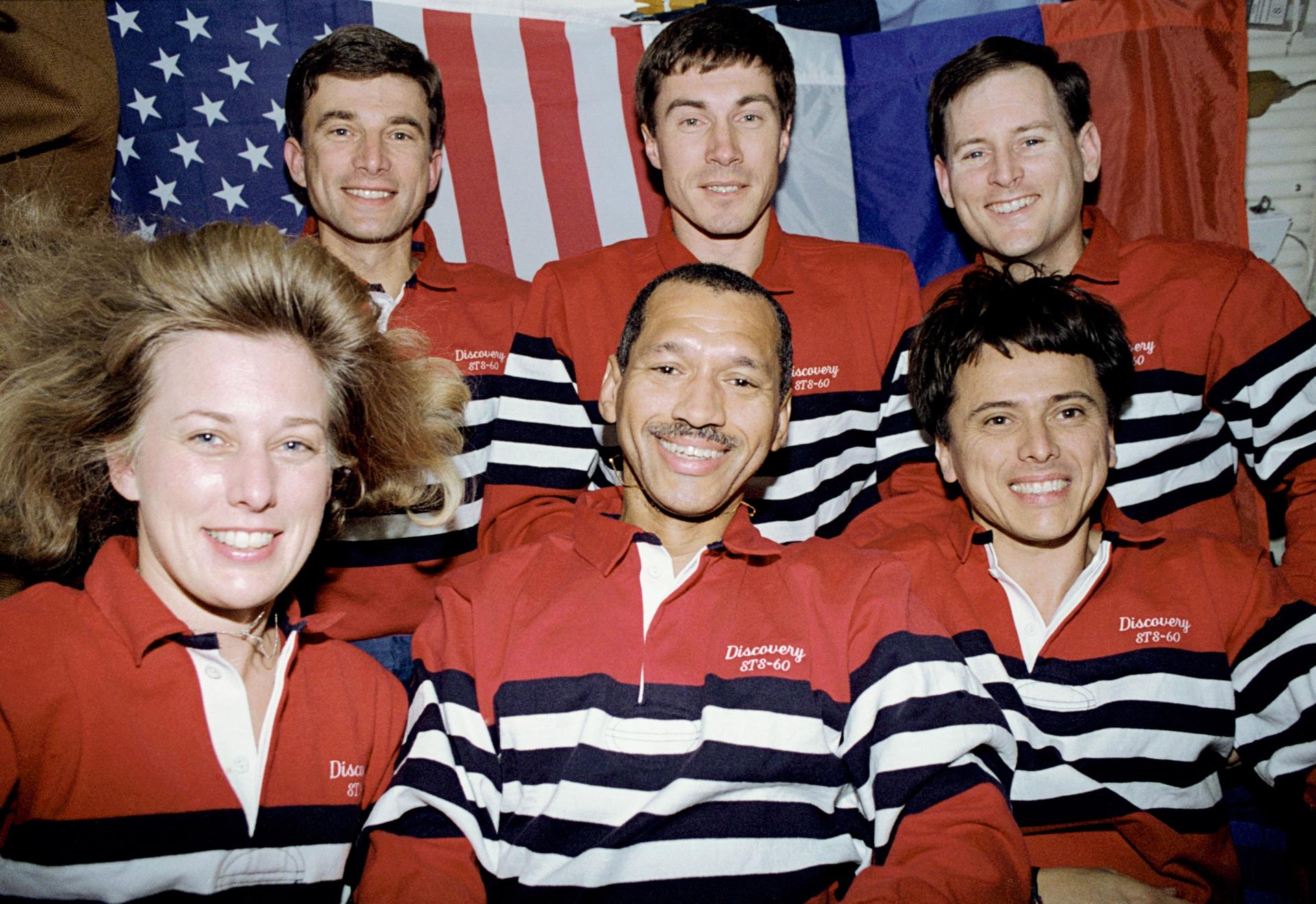 The six-member STS-60 crew pose for the traditional in-flight crew portrait, with American and Russian flags forming the backdrop on the space shuttle Discovery’s middeck