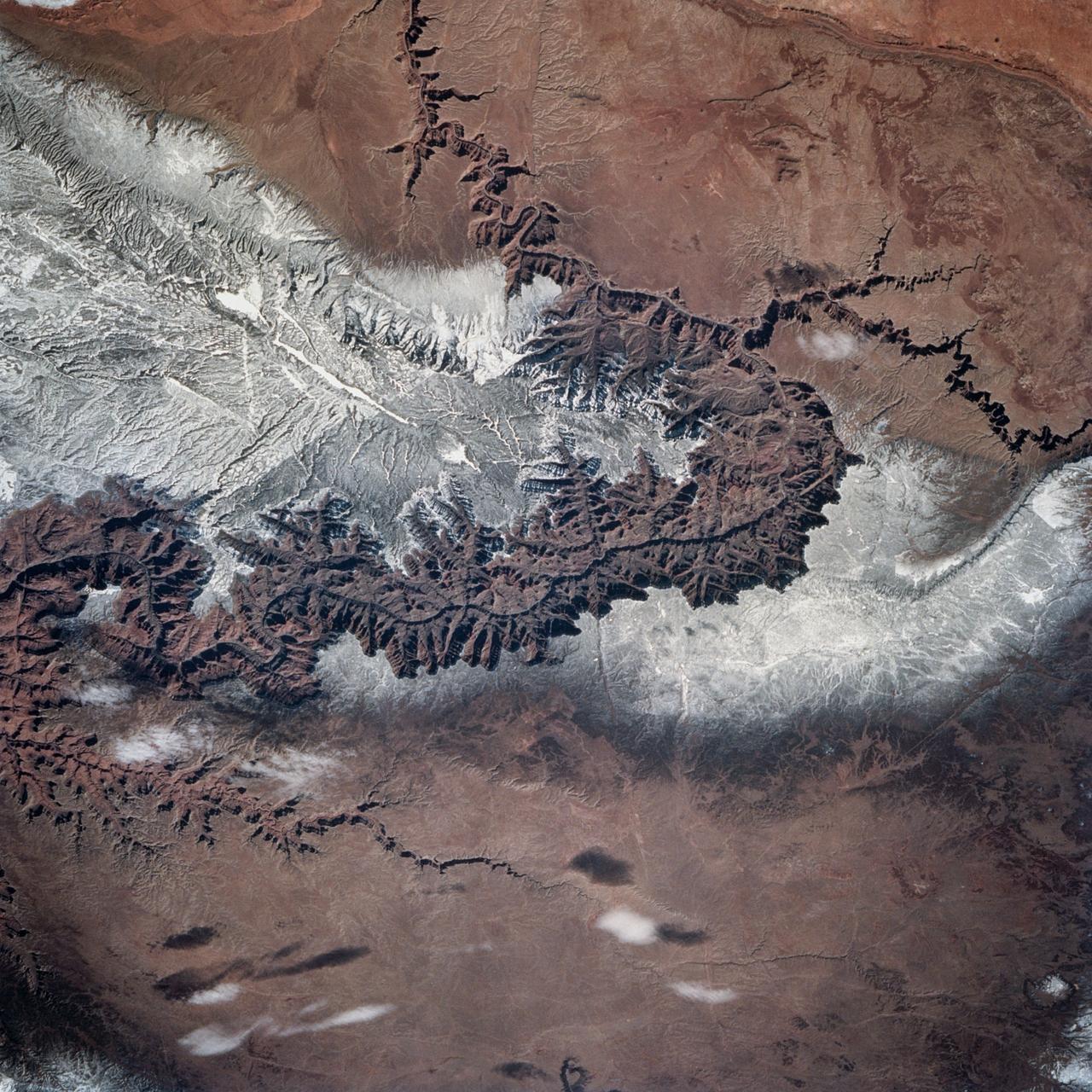 STS060-83-004 (3-11 Feb 1994) --- In this winter scene of the Grand Canyon of Arizona, the canyon is particularly well revealed because snow lies on the rims of the canyon, and exits mid-right; the Little Colorado River enters from the left, joining the Colorado just upstream of its big bend.  Visitors to the South Rim can view the canyon in both the east-west and north-south reaches.  The South Rim is closer to centers of transportation so that tourists mostly see the canyon from this area, that is from about 7,000 feet.  The canyon floor lies at 2,000 feet in this sector.  The most heavily snow covered area is the highest, reaching more than 9,000 feet (bottom right).  Visitors see this protected area by hiking and mule and helicopter rides.  The ecology of this part of the Colorado has been changed since the building of a lake upstream: river water is now derived from snow melt water from the bottom of the lake.  This water is much colder than the water which used to flow through the canyon.  According to NASA scientists, the view is unusual because the snow also reveals so well the higher country around the canyon, a swath stretching from bottom right to middle left of the view.  This higher swath is an arch of uplifted rocks known as the Kaibab Plateau, raised vertically by tectonic forces in the recent geologic past.  Despite this up parching, the Colorado River managed to maintain its course to the sea by cutting an ever deeper canyon into the Plateau.  The white snow cover hides the fact that the Kaibab Plateau is thickly forested and thus appears dark green in summer, except in areas of clear-cutting.  Since the Plateau reaches altitudes of 6 to 9,000 feet, it is both cooler and moister than the surrounding lower desert floor (top and bottom in this view) - where sparse vegetation and rocky country appear as brown colors.  The zone of dark color running parallel to the snow line is all that can be seen of the pine forest on the south flanks of the Plateau.