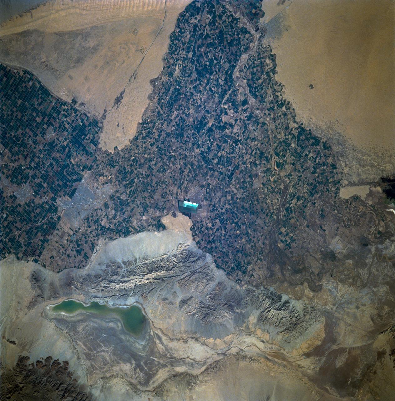 STS060-93-081 (3-11 Feb 1994)--- The Imperial Valley was documented using three films - color visible (seen here), the American infrared film (Kodak Aerochrome 2443), and the Russian panchromatic infrared film (SN-10).  Results of this test still await detailed science analysis.  However it does appear that good data was acquired of the region, and this data will be complemented by photography acquired by the Mir cosmonauts.  In this frame, the U.S.-Mexico border goes from the upper left to the middle right.  It is discernible as a vegetation line between Calexico, California and Mexicali, Mexico.  The darker vegetation north of that line is due to different agricultural practices, heavier uses of fertilizers and pesticides, and lined (tiled) agricultural fields allowing subterraneean runoff of saline irrigation runoff.  South of the line, the more polluted water draining out of the U.S. agricultural areas into the Mexican area has resulted in higher soil salinities and a consequent reduction in agricultural productivity.  At the center of the frame, a large settling and desalinization plant has been built to attempt to purify, to some degree, the polluted irrigation waters draining south out of California.  The All-American Canal, which brings in water from the Colorado River (off the frame, to the right), is located in the middle right hand portion of the frame.  To the upper left is the normally dry Laguna Salada.