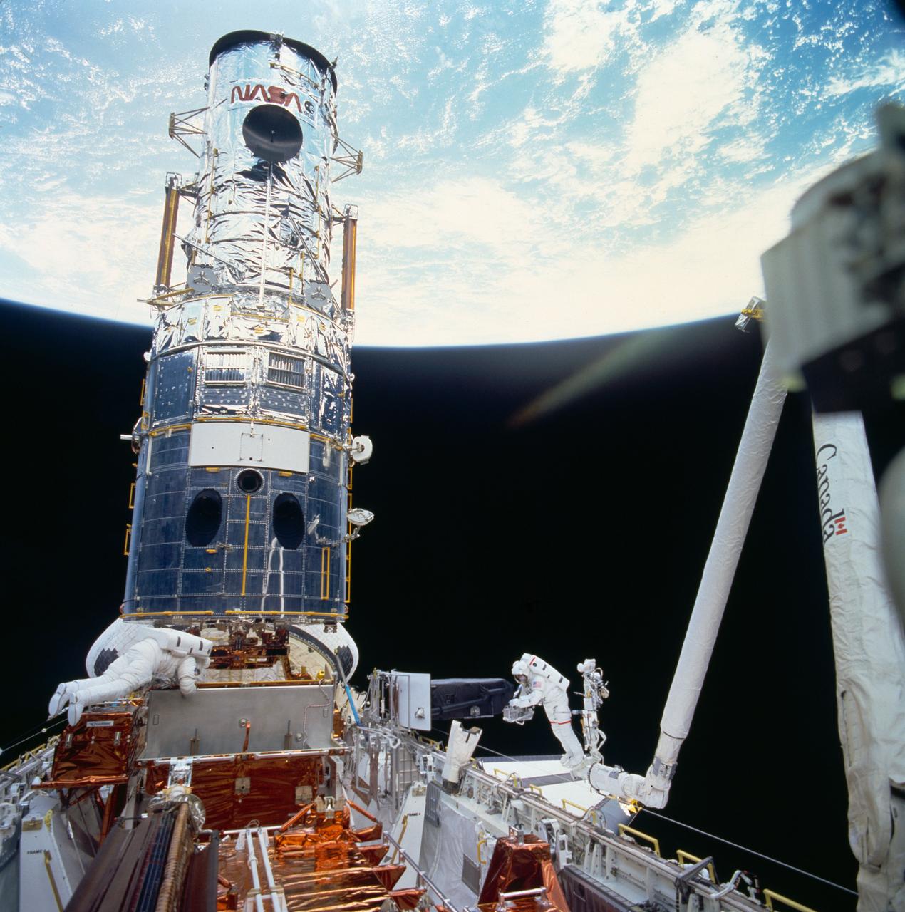 STS061-77-078 (7 Dec 1993) --- Astronaut Jeffrey A. Hoffman, anchored on the end of the Remote Manipulator System (RMS) arm, is pictured with the Wide Field/Planetary Camera (WF/PC I) during the third of five extravehicular activity?s (EVA).  Astronauts Hoffman and F. Story Musgrave, seen near the stowage area for the WF/PC, had earlier installed the new camera (note white rectangle) on lower portion of telescope.