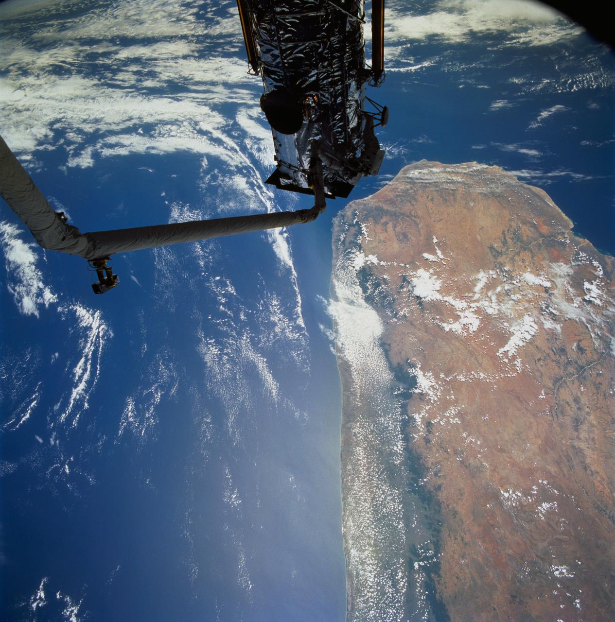 STS061-77-102 (7 Dec 1993) --- Astronauts Jeffrey A. Hoffman (left) and F. Story Musgrave are partially silhouetted against the Indian Ocean as they work to install the Magnetic Sensing System (MSS) on the Hubble Space Telescope (HST).  Musgrave is anchored to the end of the Space Shuttle Endeavour's Remote Manipulator System (RMS) arm.  The HST is positioned along the southern end of Madagascar, 325 nautical miles away.  Visible on the western coast are the sediment laden Onilahy and Fiherenana Rivers which empty into Saint Augustin Bay.  North of Fiherenana River is the Mangoky River.  The circular feature on the southern end of Madagascar and to the right of HST is the L'ivakoany Mountains.  The eastern coast is relatively straight compared to the western coast.