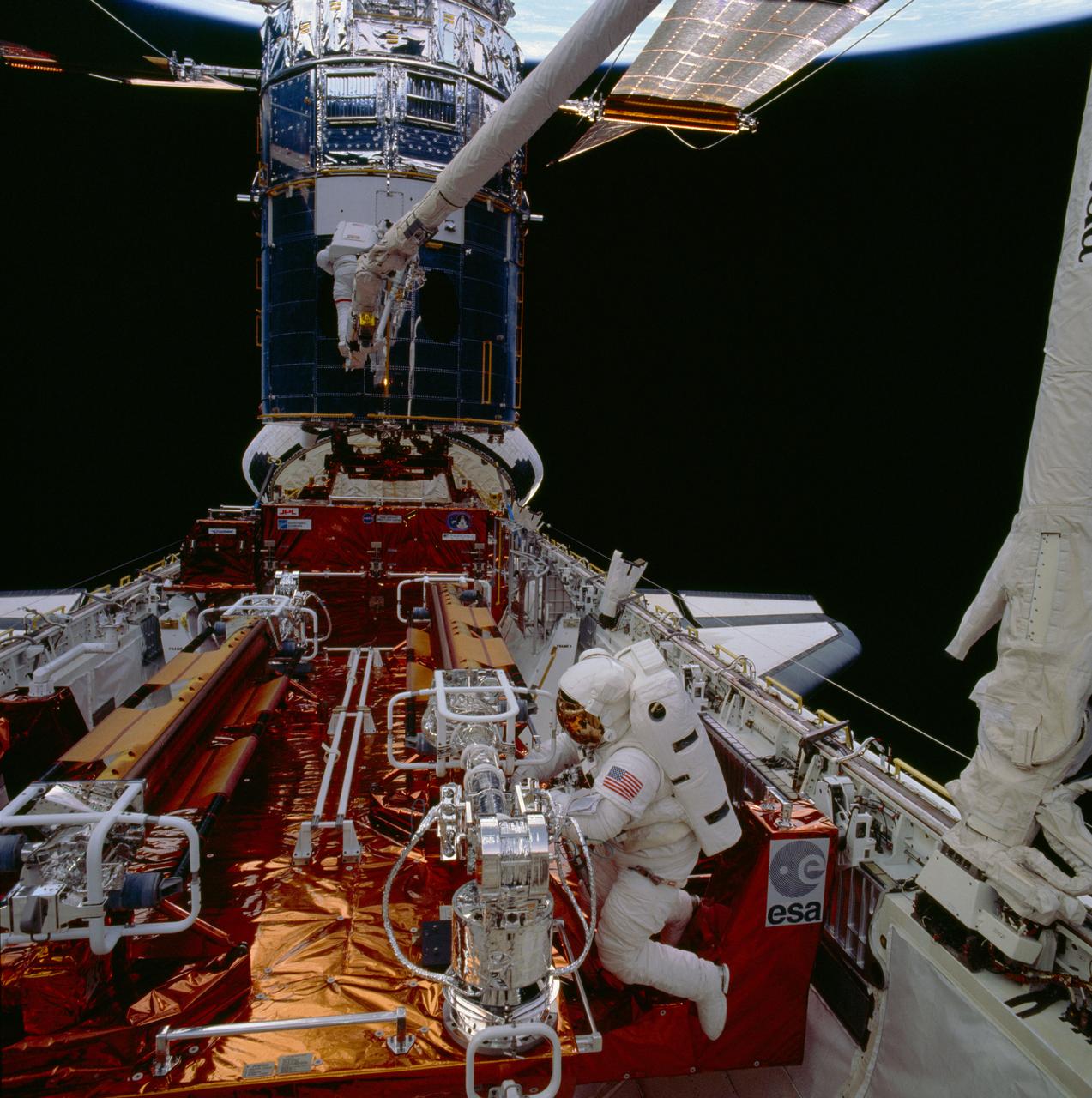 STS061-86-048 (5 Dec 1993) --- Astronauts F. Story Musgrave (foreground) and Jeffrey A. Hoffman are pictured near the end of the first of five extravehicular activity?s (EVA).  Musgrave works at the Solar Array Carrier (SAC) in the Space Shuttle Endeavour's cargo bay.  Hoffman, anchored to a foot restraint mounted on the end of the Space Shuttle Endeavour's Remote Manipulator System (RMS) arm, waits to be maneuvered to the forward payload bay.  The original solar array panels are partially visible at top, while their replacements remain stowed in foreground.  The crew's second pair of space walkers -- astronauts Kathryn C. Thornton and Thomas D. Akers -- later changed the solar arrays on the mission's second EVA.