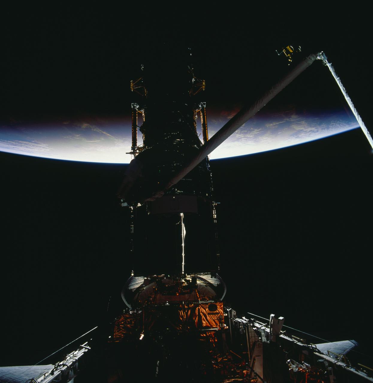 STS061-98-0AR (8 Dec 1993) --- Earth is partially illuminated but the Hubble Space Telescope (HST) and the Space Shuttle Endeavour are still mostly in darkness, in this 70mm frame photographed during the fourth of five space walks.  Astronaut Kathryn C. Thornton, barely visible above left center in the frame, works to install the Corrective Optics Space Telescope Axial Replacement (COSTAR).