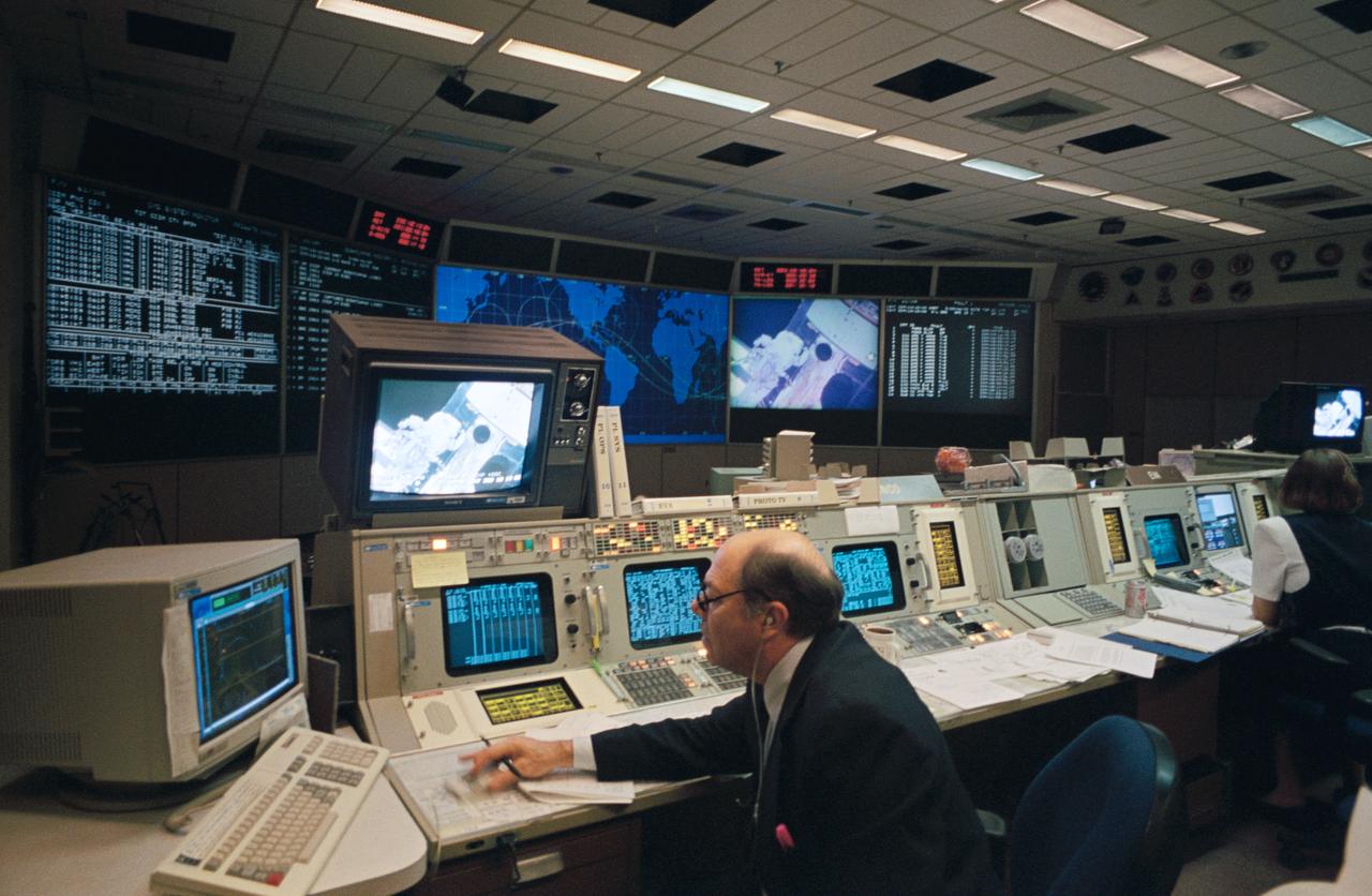 Joseph Fanelli, at the Integrated Communications Officer console, monitors the televised activity of Astronauts Story Musgrave and Jeffrey A. Hoffman. The vetern astronauts were performing the first extravehicular activity (EVA-1) of the STS-61 Hubble Space Telescope (HST) servicing mission.