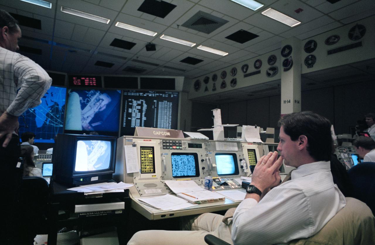 STS61-S-101 (8 Dec 1993) --- Astronaut Gregory J. Harbaugh, spacecraft communicator (CAPCOM), observes as two astronauts work through a lengthy period of extravehicular activity (EVA) in the cargo bay of the Earth-orbiting Space Shuttle Endeavour.  Seen on the screen in the front of the flight control room, preparing to work with the Hubble Space Telescope's (HST) magnetometers, are astronauts F. Story Musgrave and Jeffrey A. Hoffman.  Harbaugh stayed busy passing up flight controllers suggestions and directions during the record-breaking battery of in-space servicing sessions.  Lead flight director Milt Heflin is partially visible at left edge of frame.