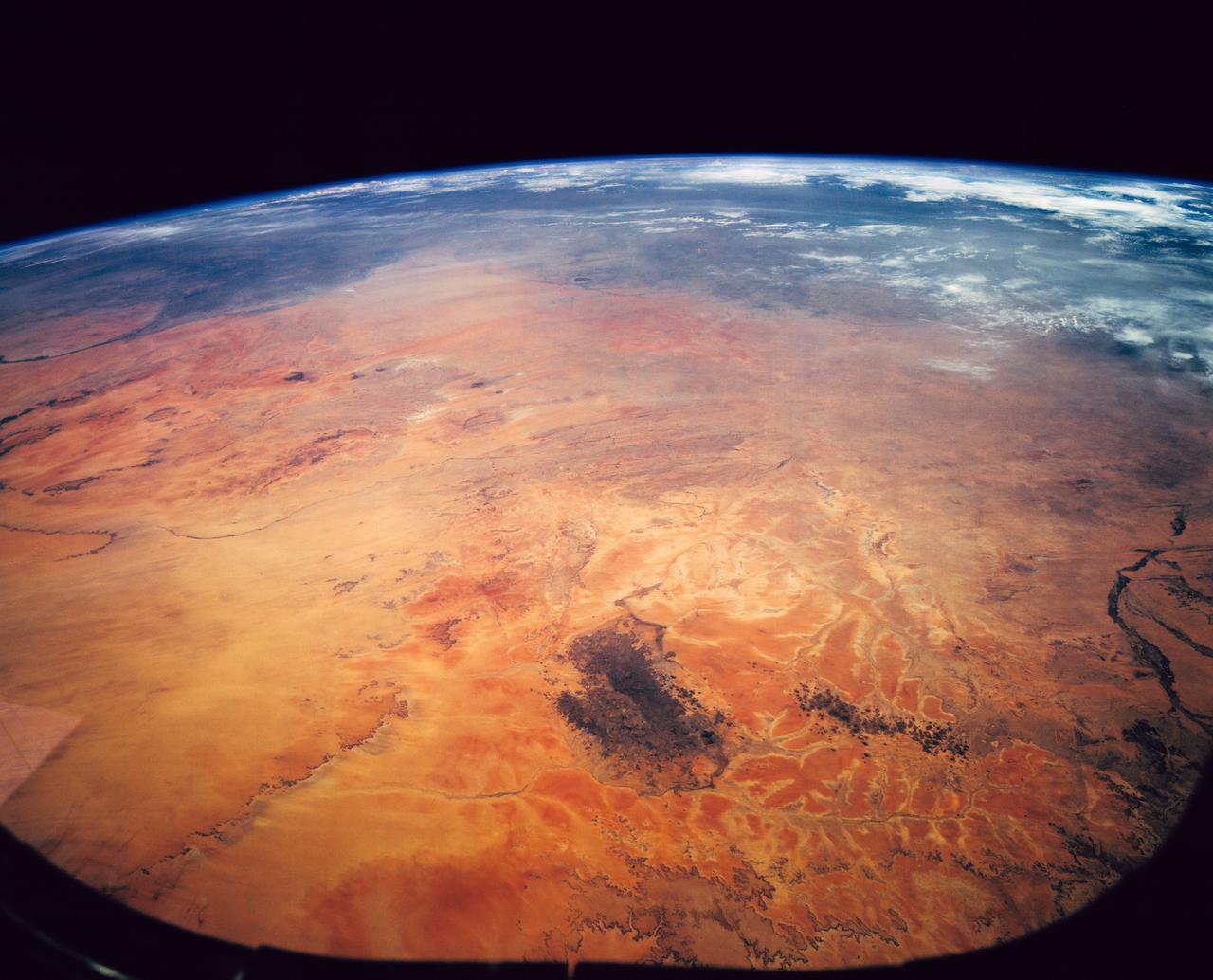 STS062-151-182Z (4-18 March 1994) --- This east-looking view shows most of the east-west extent of the country of Sudan.  The foreground shows a vegetation-less and almost uninhabited region of northwest Sudan.  The rich earth colors are ancient soils (browner and redder tones), a concentrated mass of what may be volcanic cinder cones (dark brown dots - center) and dune and younger river sediments (yellows).  The photo would have been difficult to locate had it not been for two recognizable features in the background: a visually well-known inselberg ("island mountain" -- top center) on a large west-bank tributary of the White Nile; and the confluence of the Blue and White Nile's, with the great cotton developments of the Gezira Scheme between them (top left).  The Red Sea coast is almost obscured by a dust cloud but can be discerned running across the top of the picture.  The clouds at top may be developing over the coastal ranges of Saudi Arabia beyond the Red Sea.