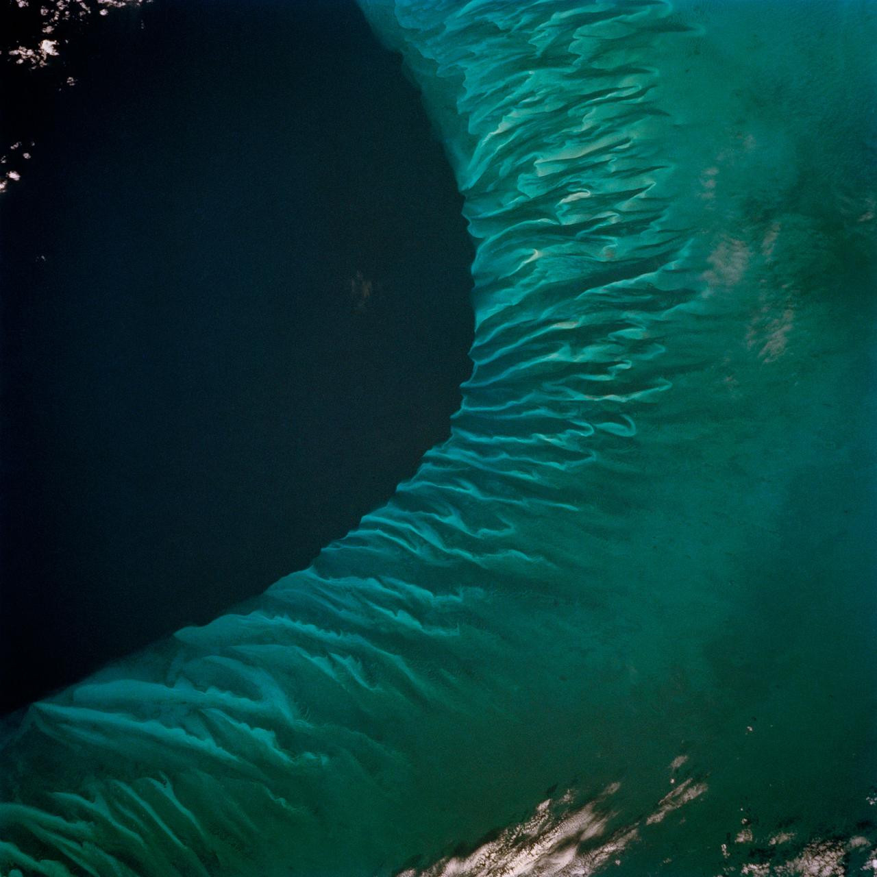 STS062-85-031 (4-18 March 1994) --- The shallow platforms (bright blue) and deep channels (dark blue) of the Bahamas provide a striking visual from space.  On a finer scale, delicate patterns are created by the islands, sandbars and tidal channels.  This view features a portion of the Tongue of the Ocean, one of the large deep water sounds in the western Bahamas.  On the platform along the edge of the Tongue of the Ocean are convoluted sandbars bordering channels which fall into the deeper water.  These channels provide an avenue for transport of sediment off the shallow platform (3-10 meters) into the deeper water (1,800 meters).