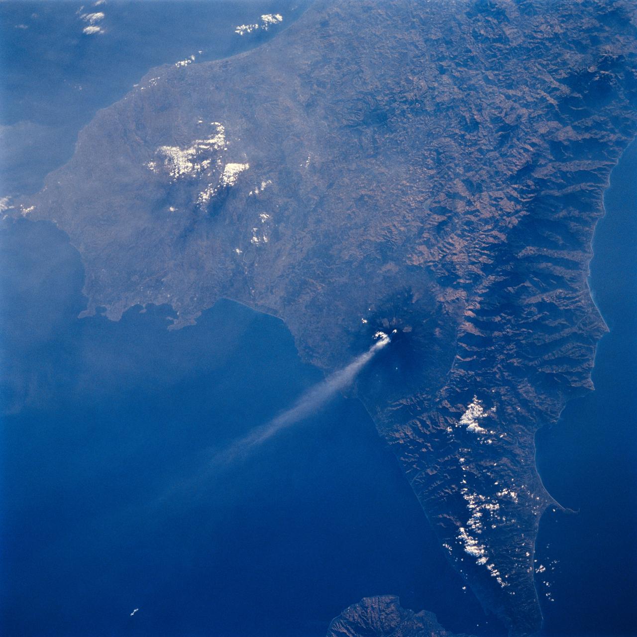 STS064-71-037 (9-20 Sept. 1994) --- Mt. Etna on Sicily displays a steam plume from its summit. Geologists attribute the volcano's existence to the collision of tectonic plates. Unlike the sudden, explosive eruption at Rabaul, Mt. Etna's activity is ongoing and is generally not explosive - Etna's slopes have been settled with villages and cultivated land for centuries. Other Mediterranean volcanoes (like Santorini) have experienced large catastrophic eruptions. Etna recently finished a two-year eruption (ending in 1993), marked by relatively gentle lava flows down the eastern flank. It has been continually degassing since then, according to the geologists, producing an omnipresent steam plume, as seen here. The 1993 flow is difficult to identify in this image because it lies within shadows on the eastern flank, but small cinder cones on the western flank mark earlier episodes of volcanic activity. Photo credit: NASA or National Aeronautics and Space Administration