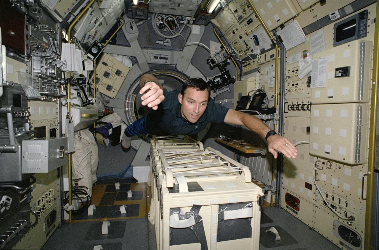 STS-65 Mission Specialist Carl E. Walz floats above center aisle equipment in the International Microgravity Laboratory 2 (IML-2) spacelab science module. Walz has just entered the IML-2 module via the spacelab tunnel (note hatch opening behind him). The tunnel connects the IML-2 module with Columbia's, Orbiter Vehicle (OV) 102's, crew compartment. Walz along with five other NASA astronauts and a Japanese payload specialist spent more than two weeks in Earth orbit conducting IML-2 experiments. This photo was among the first released by NASA following IML-2.