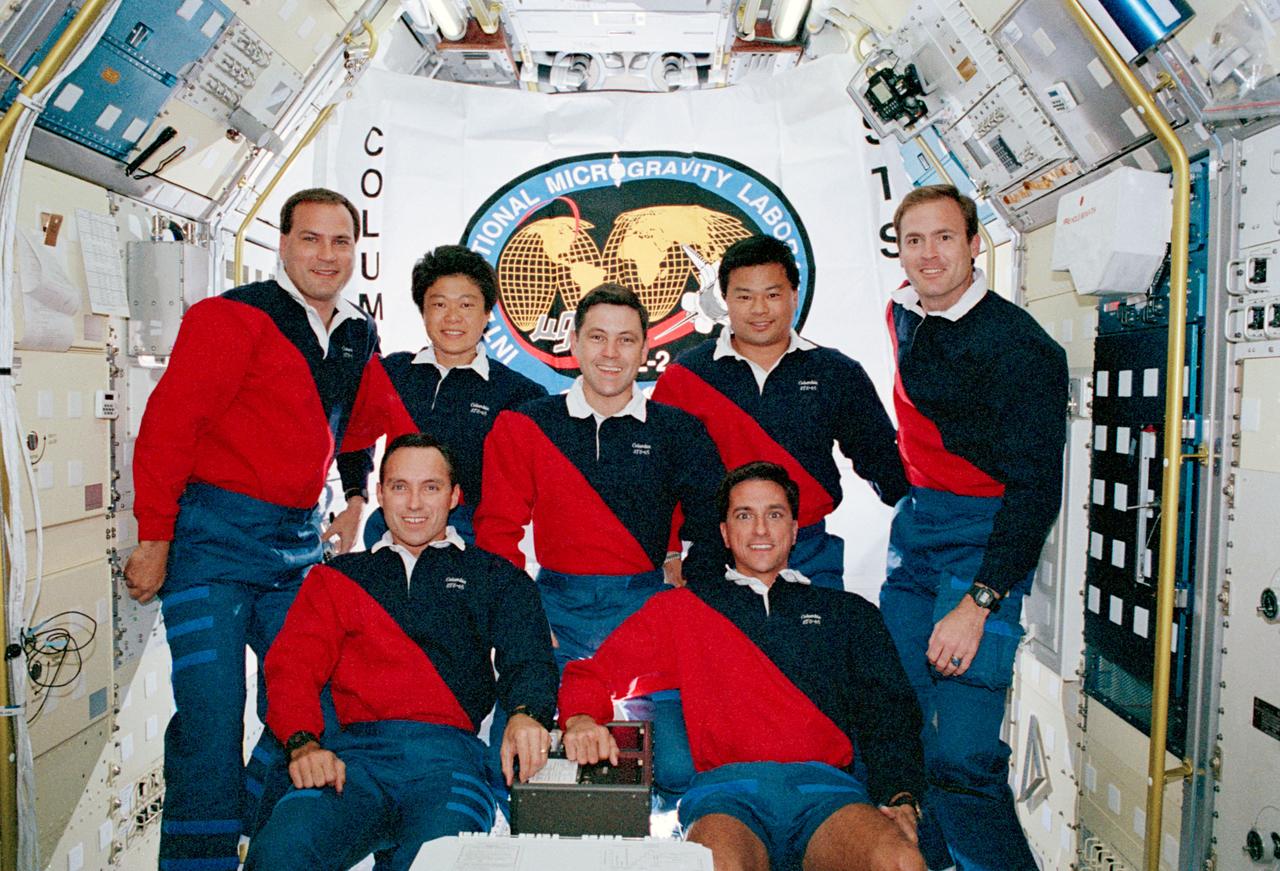 In the spacelab science module aboard the Space Shuttle Columbia, Orbiter Vehicle (OV) 102, the seven crewmembers pose for the traditional onboard (inflight) crew portrait. Displayed in the background is a flag with the International Microgravity Laboratory 2 (IML-2) insignia and Columbia inscribed along the edge. In the front row (left to right) are Mission Specialist (MS) Carl E. Walz and MS Donald A. Thomas. Behind them (left to right) are Payload Commander (PLC) Richard J. Hieb, Payload Specialist Chiaki Mukai, Commander Robert D. Cabana, MS Leroy Chiao, and Pilot James D. Halsell, Jr. Mukai represents the National Space Development Agency (NASDA) of Japan. Crewmembers are wearing their mission polo shirts for the portrait. Inside this module, the crew conducted experiments in support of the IML-2 mission.
