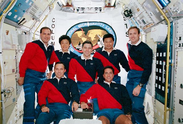 STS-65 crew onboard portrait in IML-2 spacelab module with mission flag