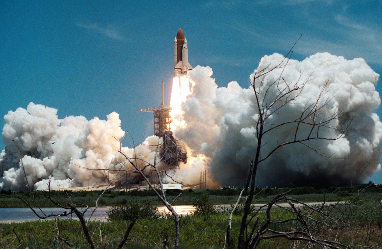 Columbia, Orbiter Vehicle (OV) 102, begins its roll maneuver after clearing the fixed service structure (FSS) tower as it rises above Kennedy Space Center (KSC) Launch Complex (LC) Pad 39A. In the foreground of this horizontal scene is Florida brush and a waterway. Beyond the brush, the shuttle's exhaust cloud envelops the immediate launch pad area. Launch occurred at 12:43 pm Eastern Daylight Time (EDT). The glow of the space shuttle main engine (SSME) and solid rocket booster (SRB) firings is reflected in the nearby waterway. Once in Earth orbit, STS-65's six NASA astronauts and a Japanese Payload Specialist aboard OV-102 will begin two weeks of experimentation in support of the second International Microgravity Laboratory (IML-2).