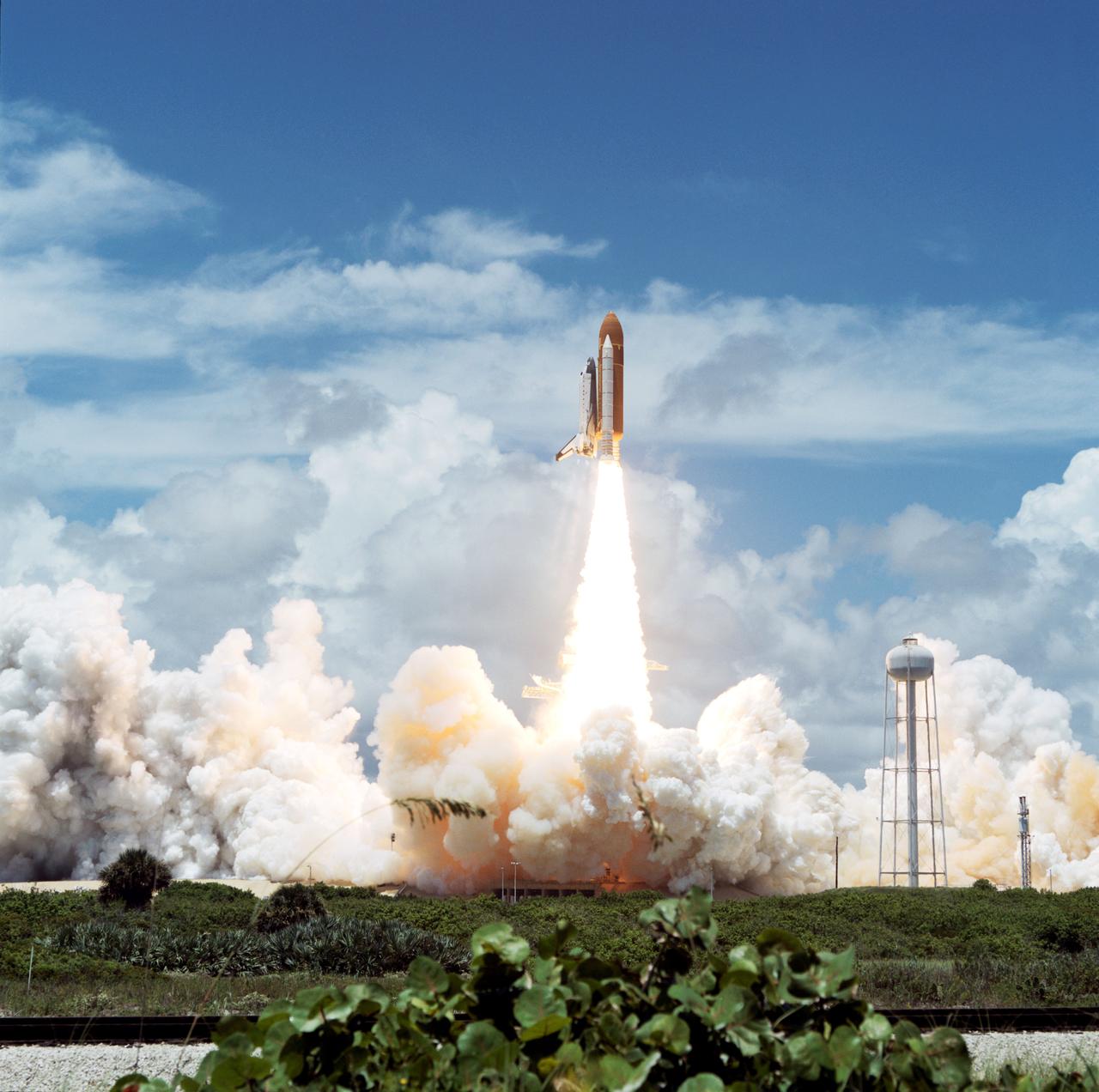 Columbia, Orbiter Vehicle (OV) 102, heads skyward after clearing the fixed service structure (FSS) tower at Kennedy Space Center (KSC) Launch Complex (LC) Pad 39A. Florida plant life appears in the foreground. The exhaust cloud produced by OV-102's solid rocket boosters (SRBs) covers the launch pad area with the exception of the sound suppression water system tower. OV-102's starboard side and the right SRB are visible from this angle. Launch occurred at 12:43 pm Eastern Daylight Time (EDT). Once in Earth orbit, STS-65's six NASA astronauts and a Japanese Payload Specialist aboard OV-102 will begin two weeks of experimentation in support of the second International Microgravity Laboratory (IML-2).