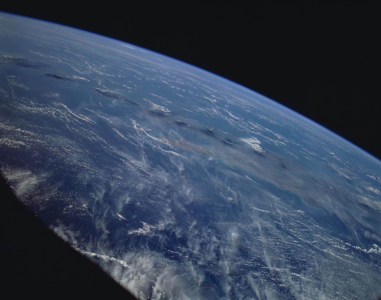 This is a striking, oblique view to the south of the Indonesian islands of Java (right), Bali and Lombok (upper left). The linear array of dark regions across the photo is a chain of volcanoes which make up the back bone of this part of the Indonesian Islands. This chain has been quite active over the past six months. Plumes of steam can be seen rising from the summits of Arjuno (west-central Java) and Merapi (central Java, near the right side of this photo). The region appears hazy due to an extended drought over Indonesia and Australia. Because of drought conditions, huge fires continue to burn over other regions of Indonesia, New Guinea and norther Australia, producing a regional smoke pall.