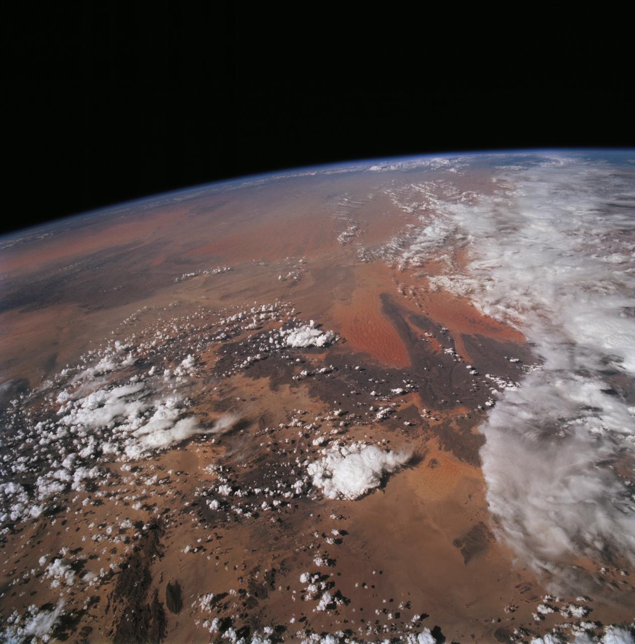 STS068-228-081 (30 September-11 October 1994) --- This northwest-looking view shows central Algeria with an unusual amount of cloud cover, responsible for one of the infrequent bouts of rain in the Sahara Desert. The lope-shaped, red sand dunes mass in the center of the view is one of the most prominent features in the Sahara as seen from the Space Shuttle Endeavour. It is known as the Tifernine Dunes. The Atlas Mountains (top) are only apparent in this view because of the clouds, which cap their summits.