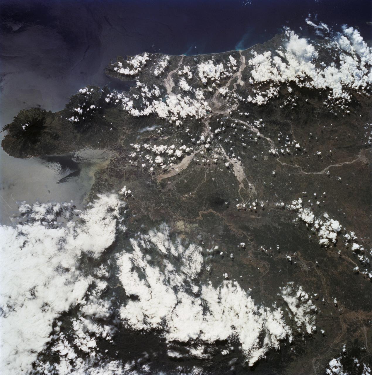 STS068-232-083 (30 September-11 October 1994) --- This is a view of Mount Pinatubo, Philippine Islands, orient with the coast to the top.  View westward across central Luzon and Mount Pinatubo.  Manilla Bay is in partial sunglint along the left edge of the frame.  The extensive flows of volcanic ash (lahars) extending from the mountain are readily seen despite partial cloud cover.  The ash is mobilized with every rain in this typhoon-ridden region, flowing down valleys, filling drainage channels, and covering fields and towns.  The STS-68 crew obtained excellent photographs of the region, for comparison to the radar data also obtained on the mission.  Photographs in sunglint have proven particularly helpful because they show the exact outlines of surface water, which provides a datum point for the radar returns.